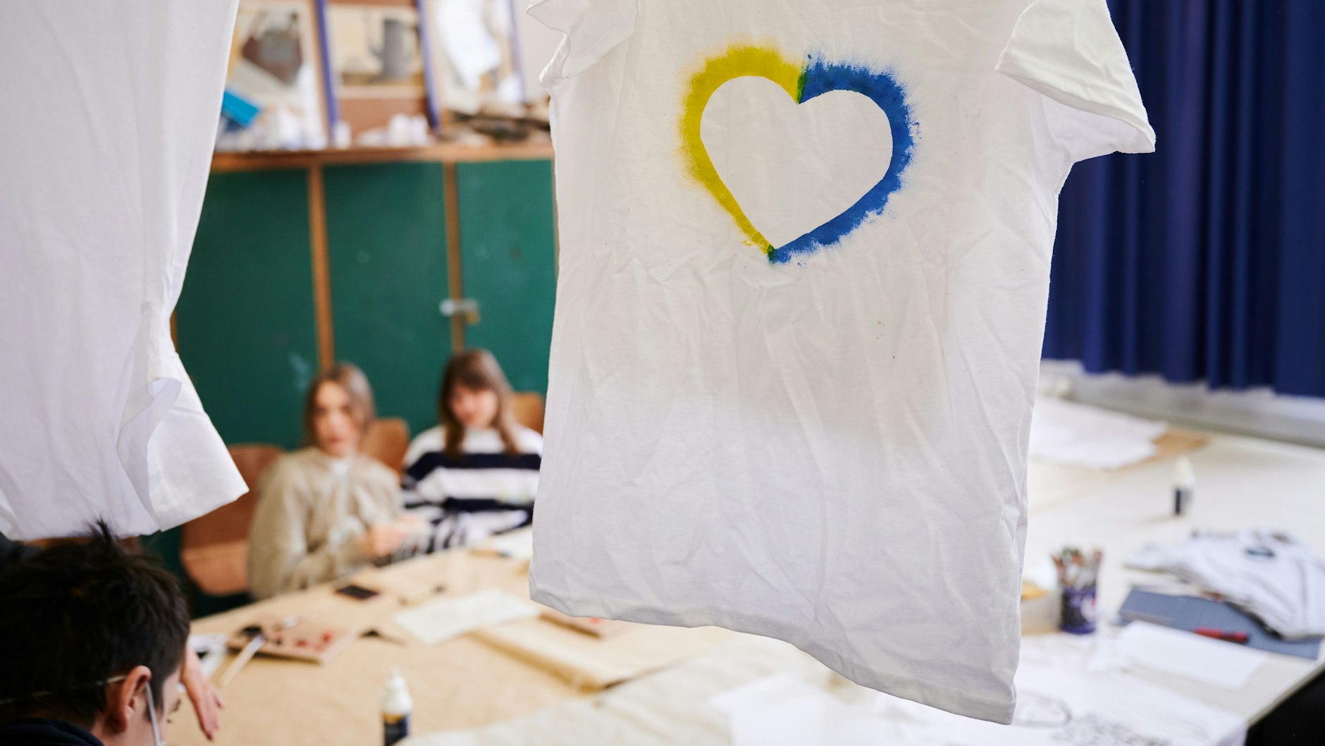 Ein T-Shirt mit einem Herz in den Farben der Ukraine hängt im Klassenraum einer Willkommensklasse am Willi-Graf-Gymnasium in Lichterfelde.