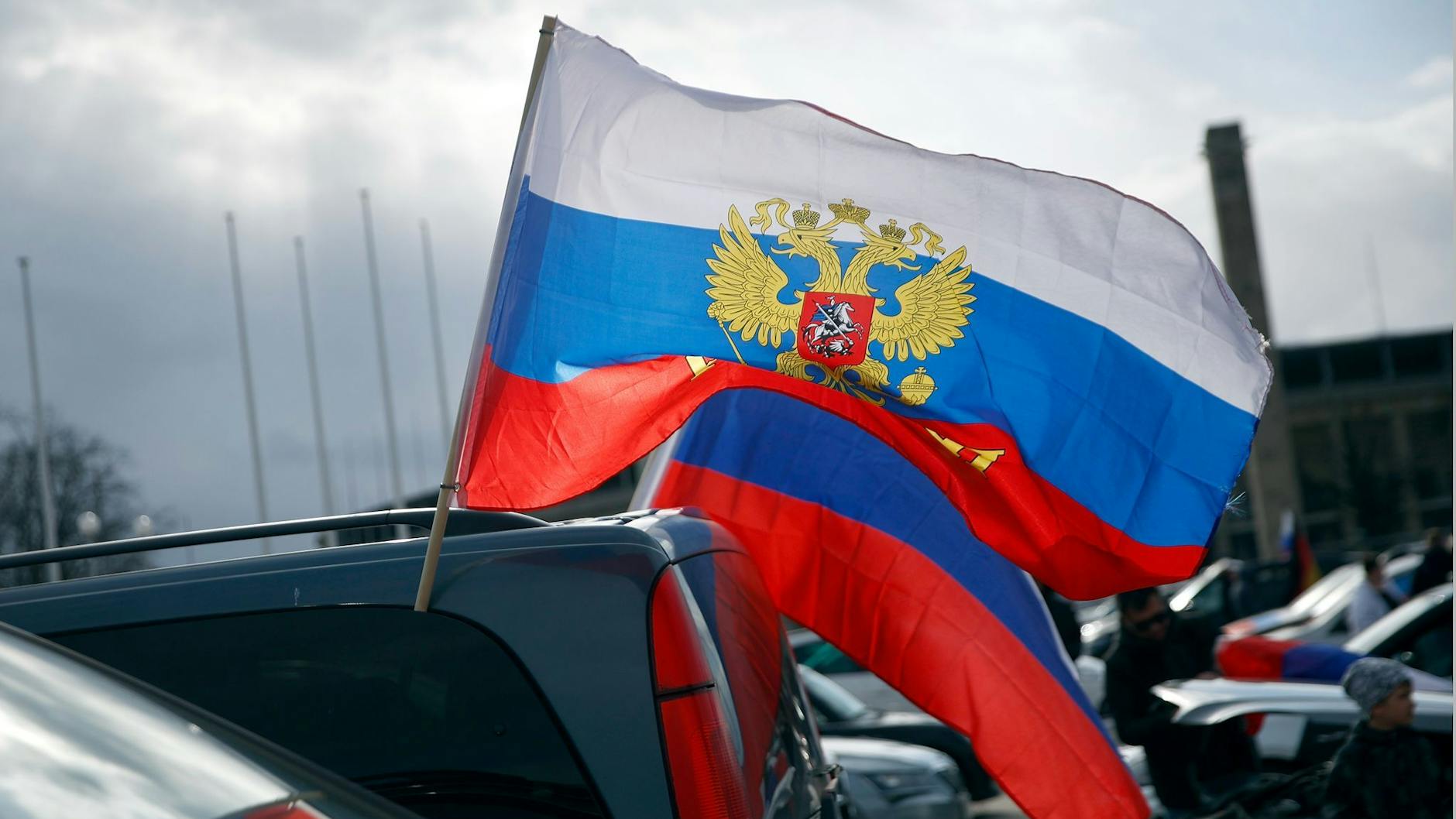 Flaggen mit den russischen Nationalfarben und dem russischen Staatswappen wehen an einem Auto.