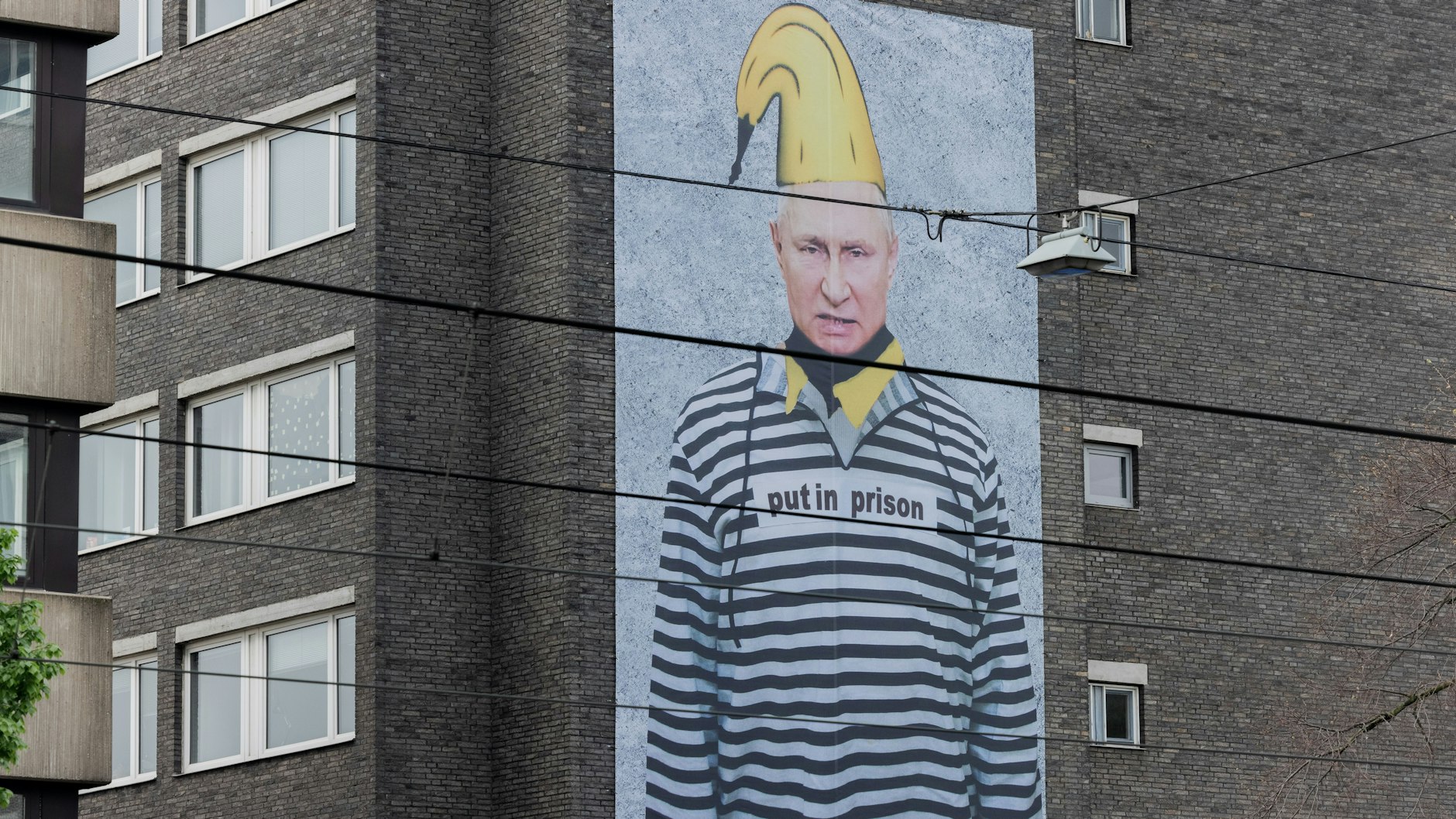 Präsidenten Putin als Sträfling mit Bananenmütze und dem Schriftzug "put in prison" (Packt ihn ins Gefängnis) an einer Hochhausfassade in Köln.
