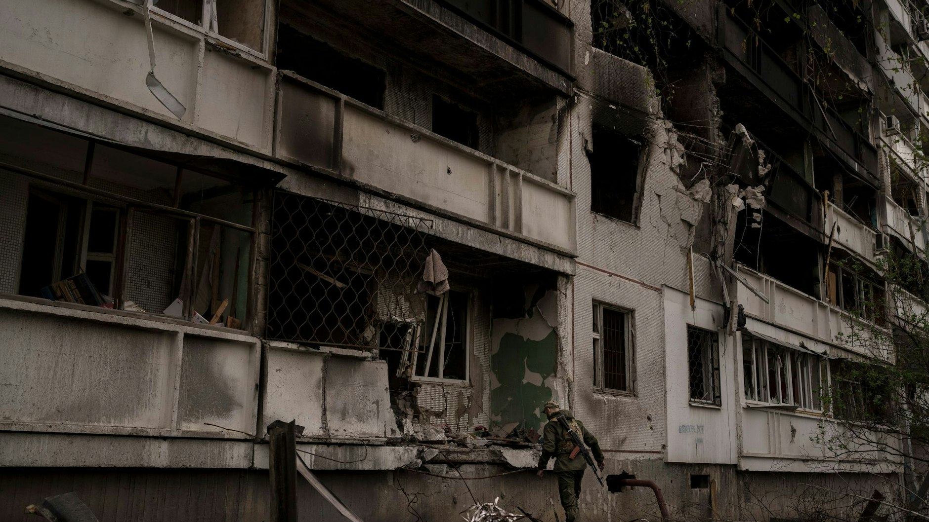 Ein ukrainischer Soldat steht nach einem russischen Angriff vor einem beschädigten Wohnhaus.