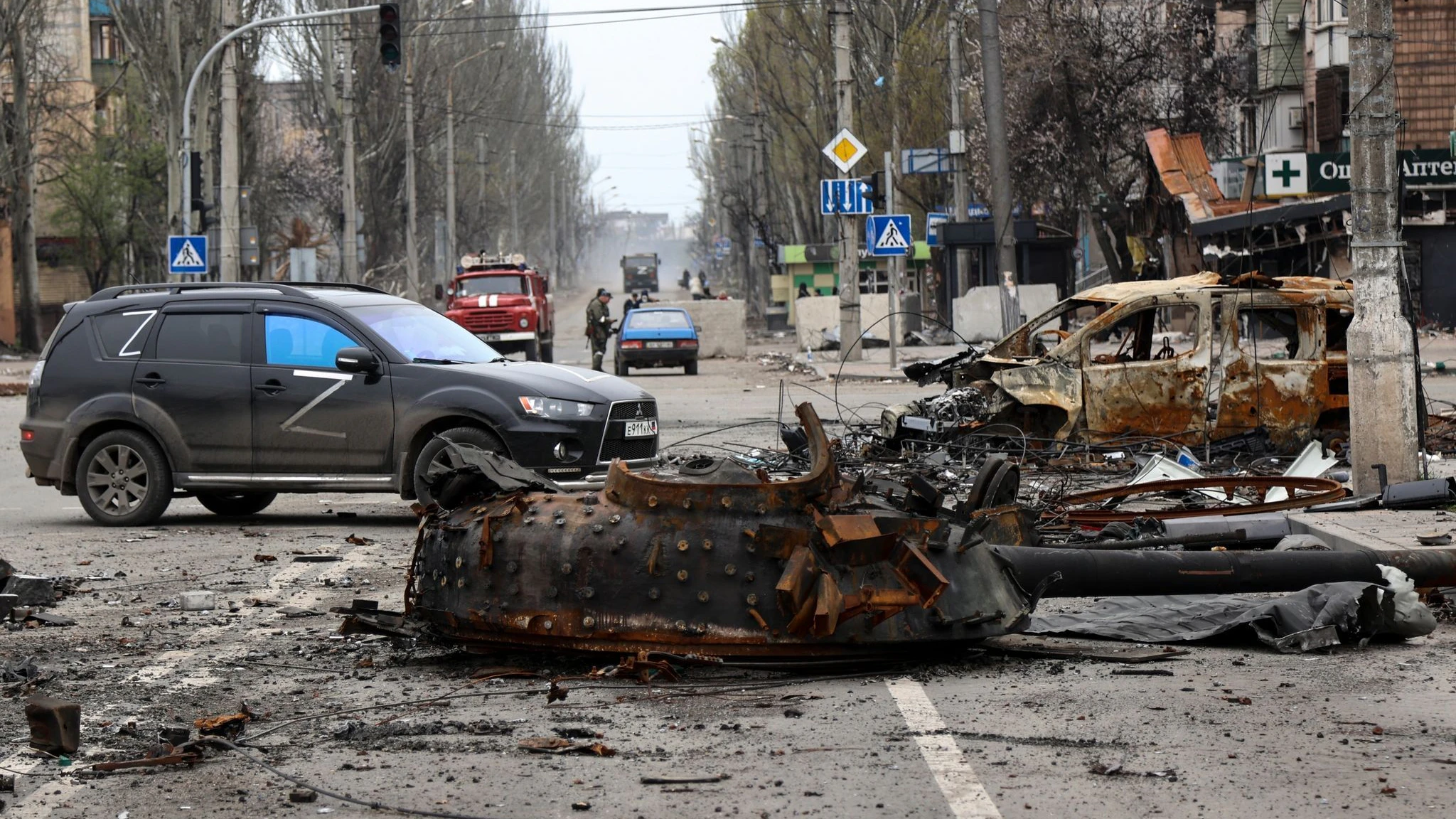 Ein Teil eines zerstörten Panzers und ein verbranntes Fahrzeug auf einer Straße in Mariupol. 