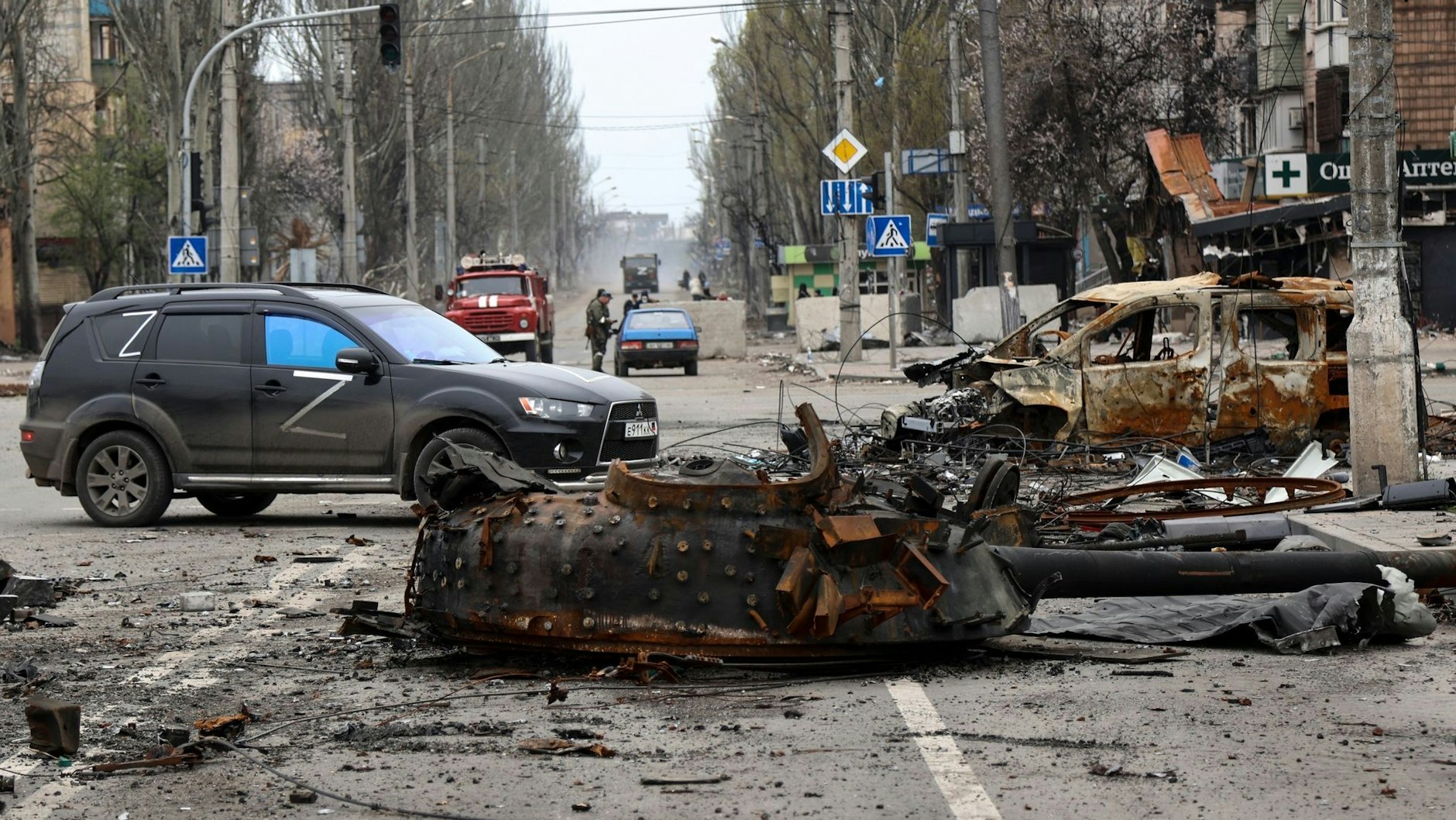 Ein Teil eines zerstörten Panzers und ein verbranntes Fahrzeug auf einer Straße in Mariupol.