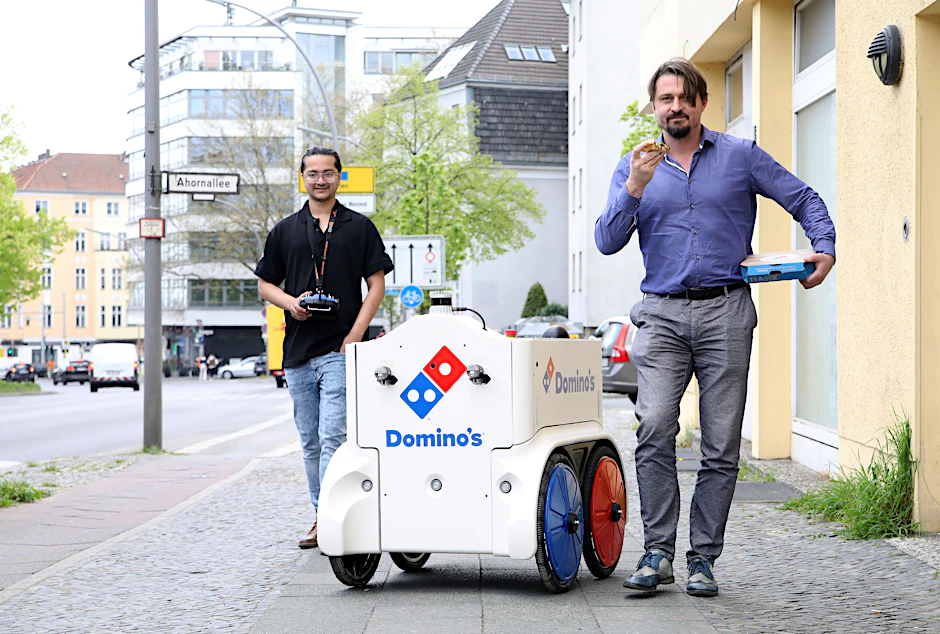 Zwei Männer und ein Roboter: Shashank Pathak überwacht die Fahrt, CEO Daniel Richart isst Pizza.