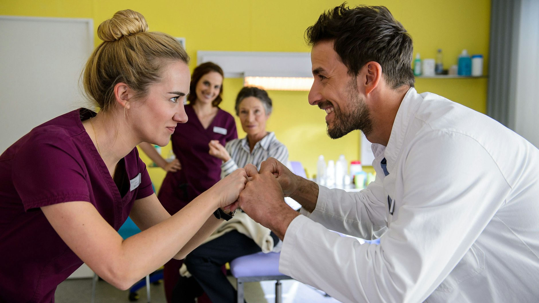 Entspanntes Betriebsklima: Pflegekraft und Klinikarzt posieren in der Serie „Bettys Diagnose“ vor einem Patientenbett.