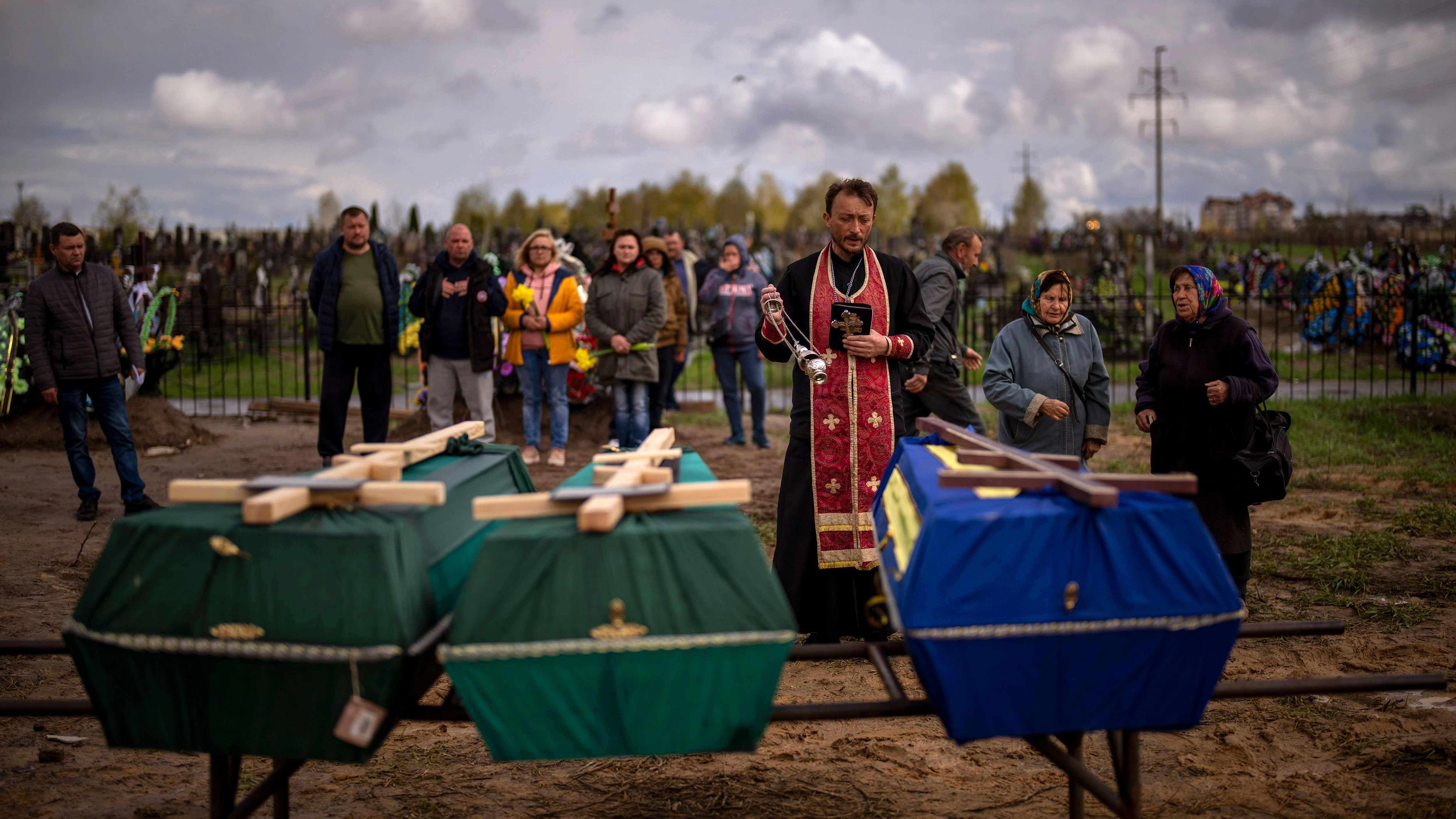 Ukraine, Butscha: Ein Priester segnet drei Verstorbene, die während der russischen Besatzung starben und aus provisorischen Gräbern in Butscha exhumiert wurden. 