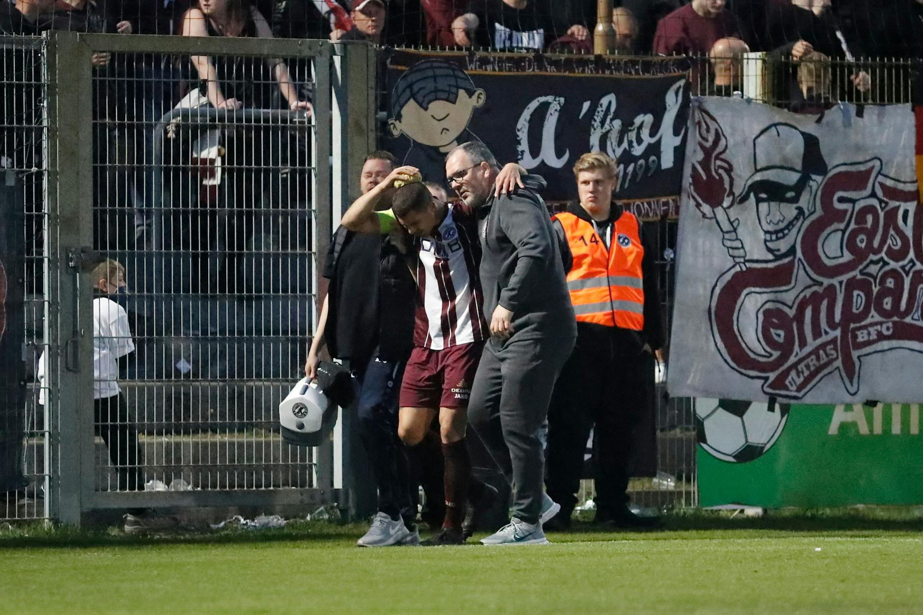 Gestützt auf Physiotherapeut Adrian Marklowski und Teammanager Jörn Lenz muss BFC-Kapitän Andreas Pollasch mit einer blutenden Platzwunde vom Platz.