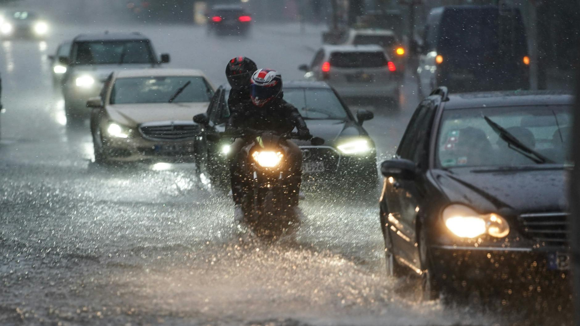 Autos und Motorräder fahren bei starkem Regen über die überflutete Friedrichstraße in Berlin-Mitte.