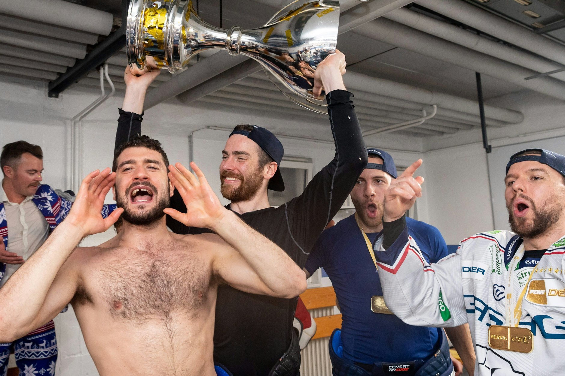 In der Kabine der Münchner Olympiahalle nahm die Meister-Party der Eisbären noch mal Fahrt auf: Giovanni Fiore jubelt oben ohne, Marcel Noebels mit dem Pokal.