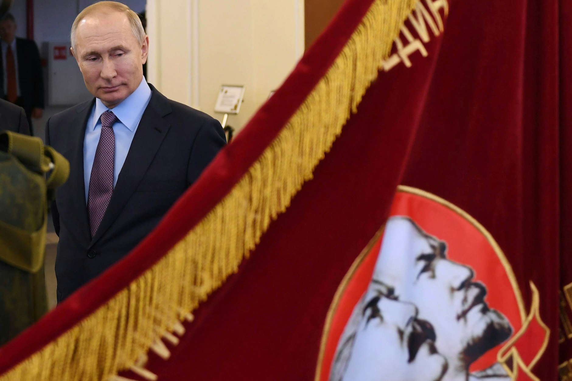 Wladimir Putin läuft an einer Flagge vorbei mit Bildern von Wladimir Lenin und Joseph Stalin.