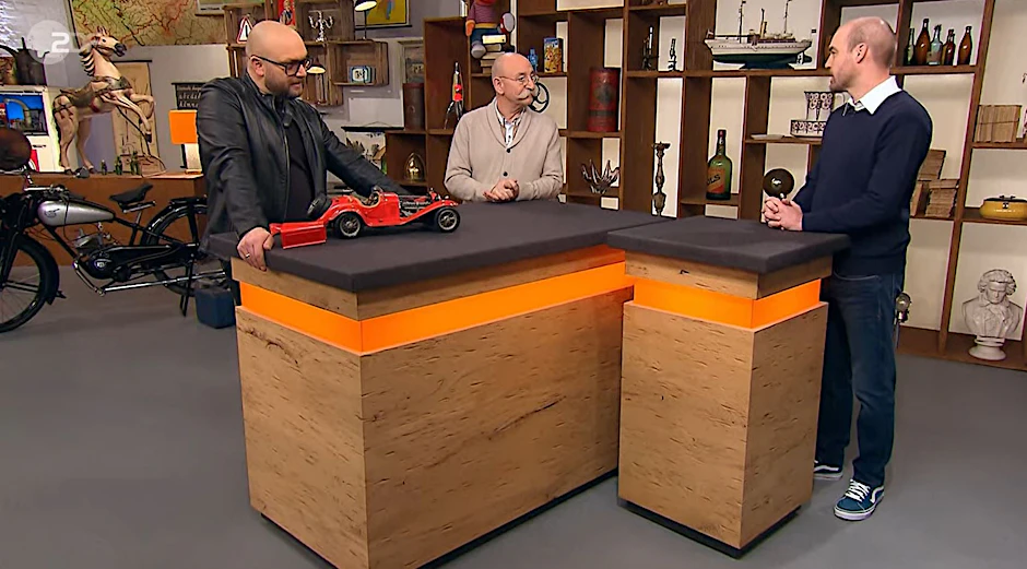 Horst Lichter, Sven Deutschmanek und Tom Eidelmann stehen bei „Bares für Rares“ um ein Modell eines Alfa Romeo 8C herum.