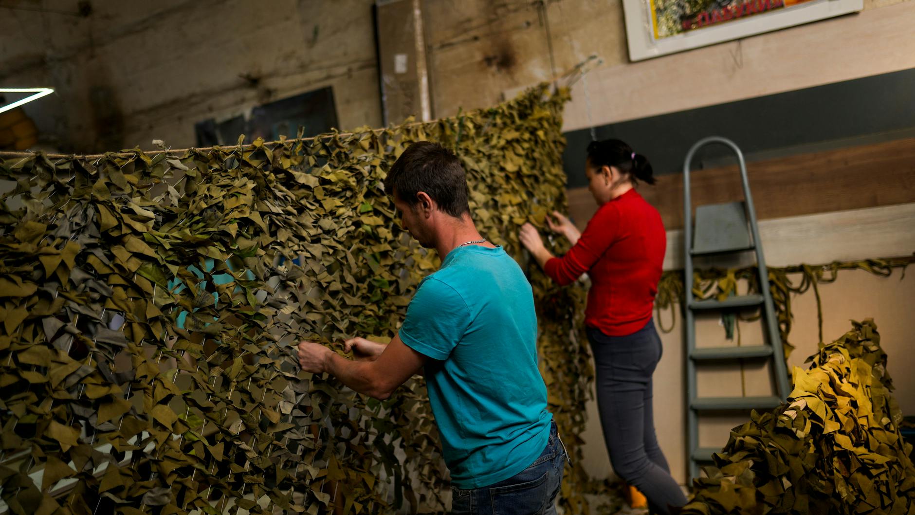 Ein Mann und eine Frau fertigen ein Tarnnetz.