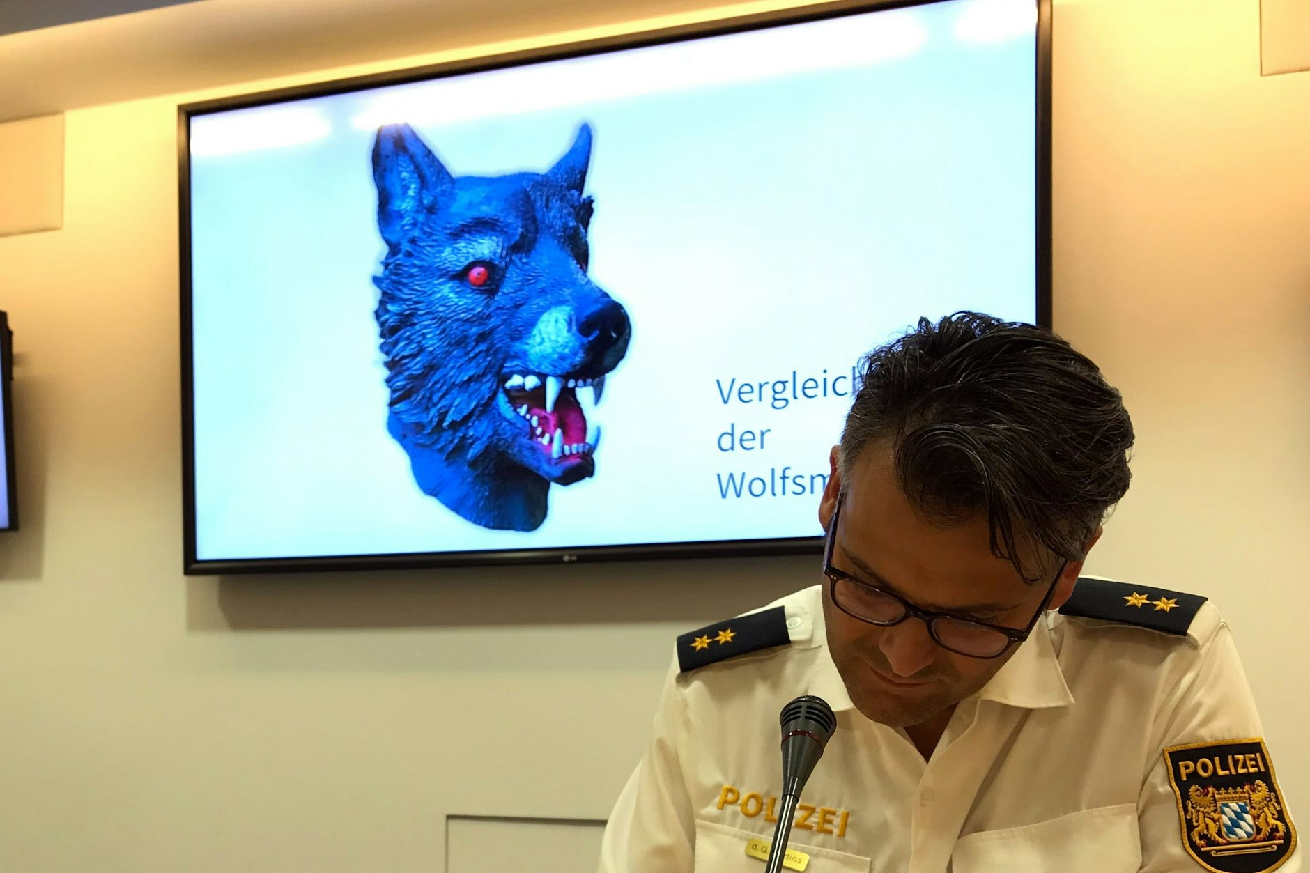 Marcus da Gloria Martins, Sprecher der Münchner Polizei, sitzt vor einem Bildschirm, auf dem die Polizei ein Vergleichsbild einer Wolfsmaske präsentiert. Mit einer solchen Maske hatte sich der Täter der Elfjährigen genähert und sie vergewaltigt.