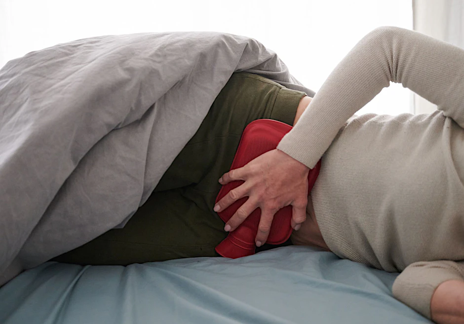 Eine Frau liegt mit Menstruationsbeschwerden im Bett (Symbolbild).
