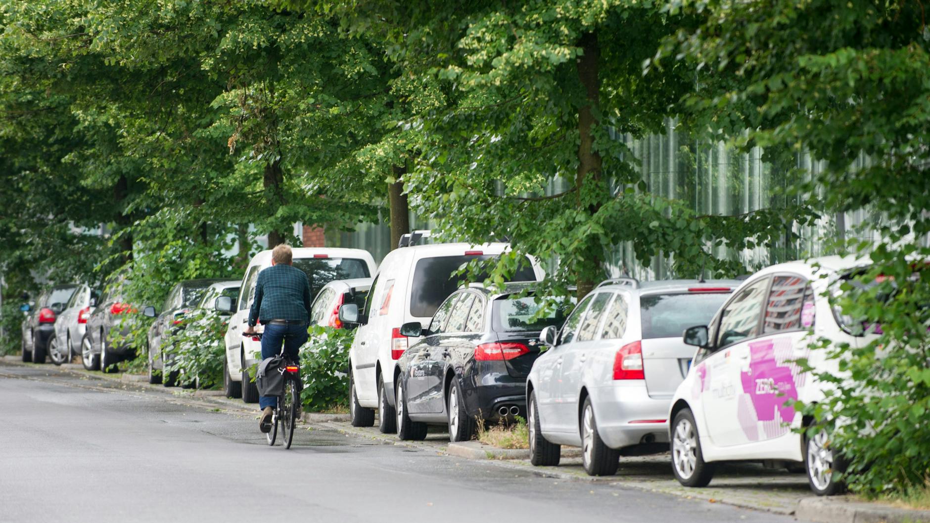 Autos parken am Straßenrand während ein Fahrradfahrer vorbeifährt.