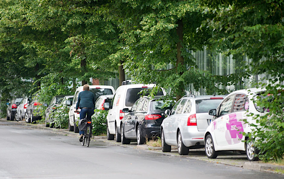 Autos parken am Straßenrand während ein Fahrradfahrer vorbeifährt.