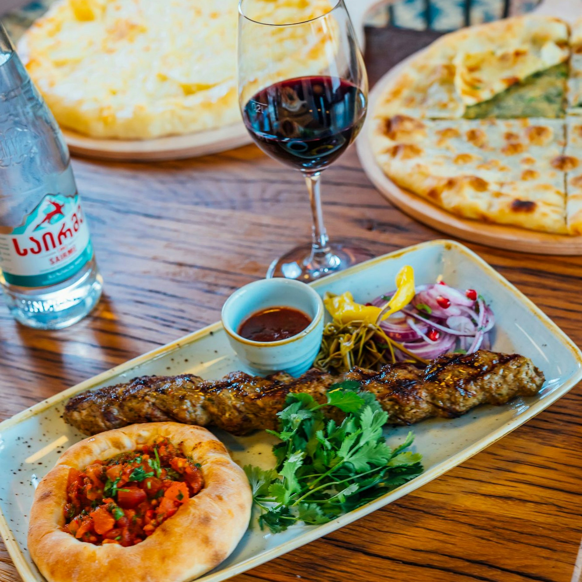 Lyulya Kebab vom Lamm mit Tomaten-Puri, marinierten Zwiebeln, eingelegter grüner Paprika und Tkemali.