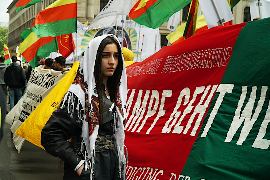 Demonstrantin steht vor Bannern des Kurdenaufzugs in Berlin.