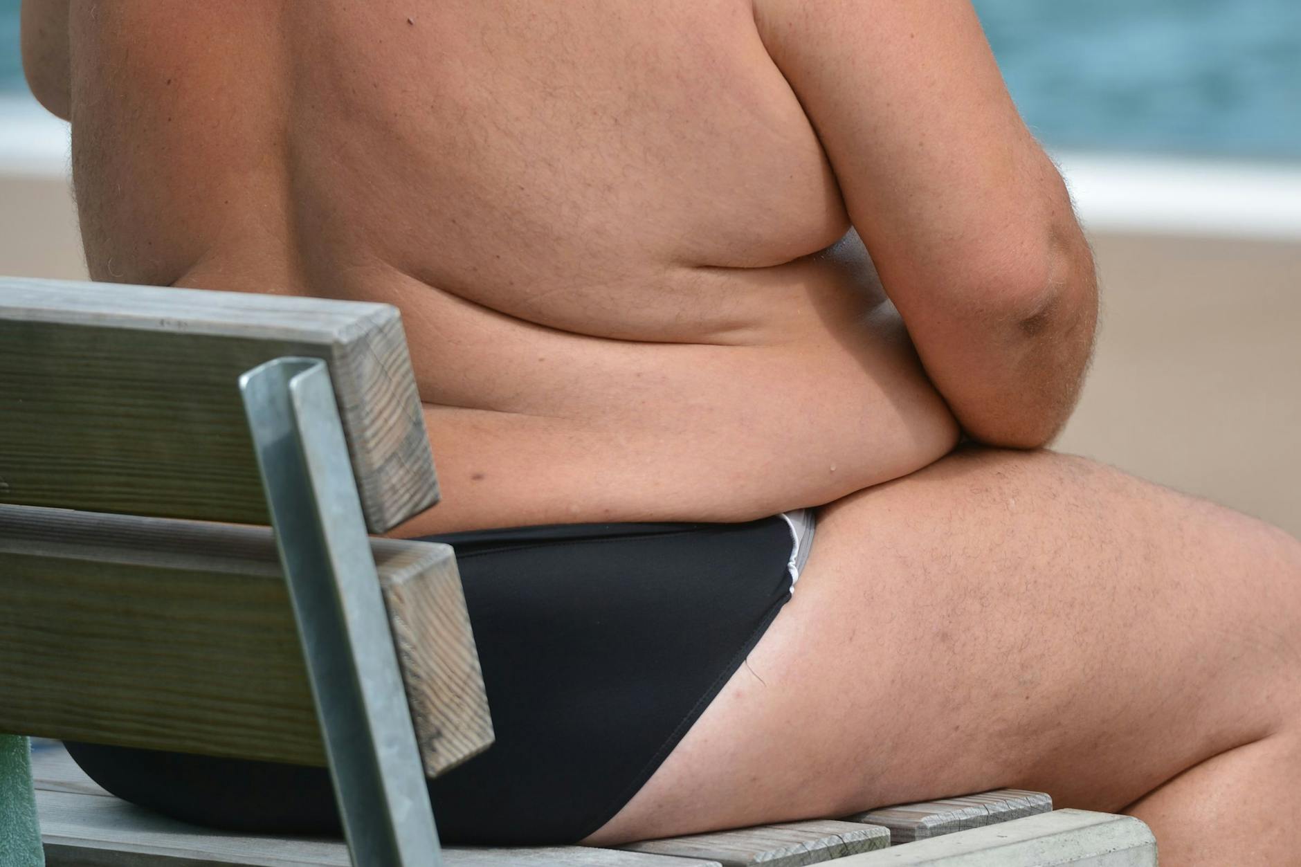 Ein übergewichtiger Deutscher sitzt in einem Freibad. 