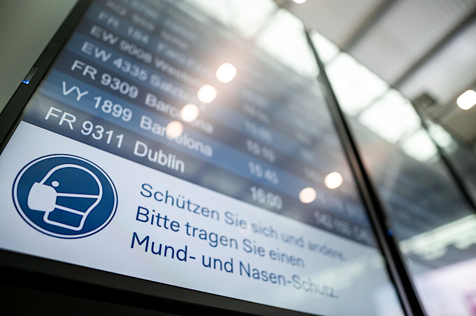 Auf einer Anzeigetafel im Flughafen Düsseldorf steht der Hinweis „Schützen Sie sich und andere. Bitte tragen Sie einen Mund- und Nasen-Schutz“