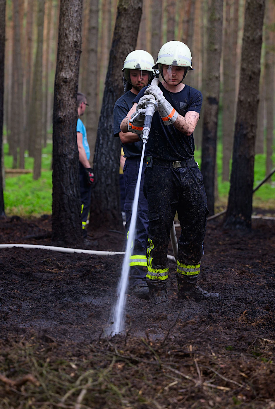 Einsatzkräfte der Feuerwehr löschen Glutnester nach einem Waldbrand.