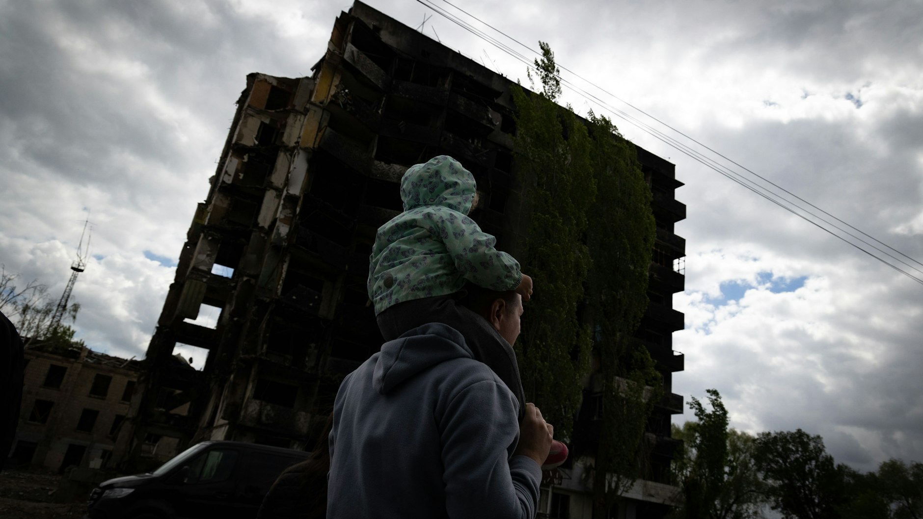 Ein Mann geht mit einem Kind an einem zerstörten Gebäude vorbei. 
