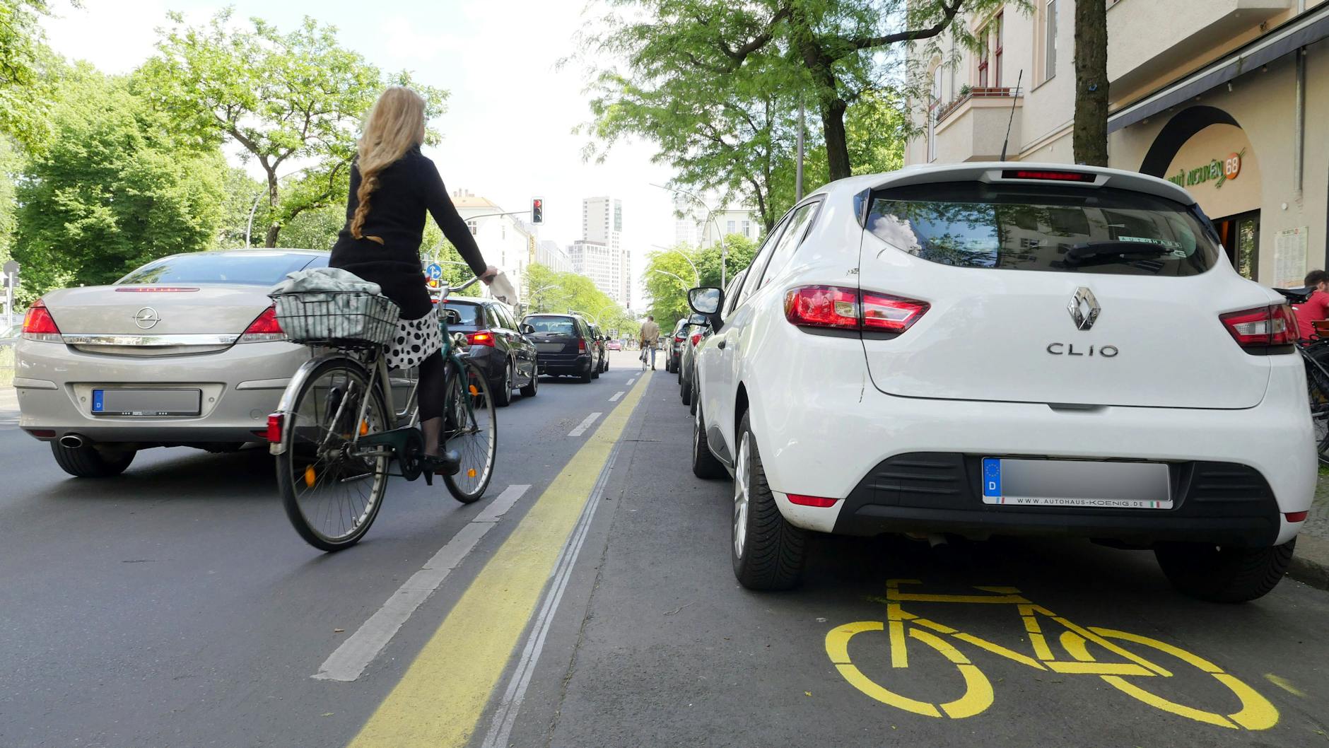 Eine Fahrradfahrerin fährt zwischen parkenden und fahrenden Autos hindurch (Archivfoto).