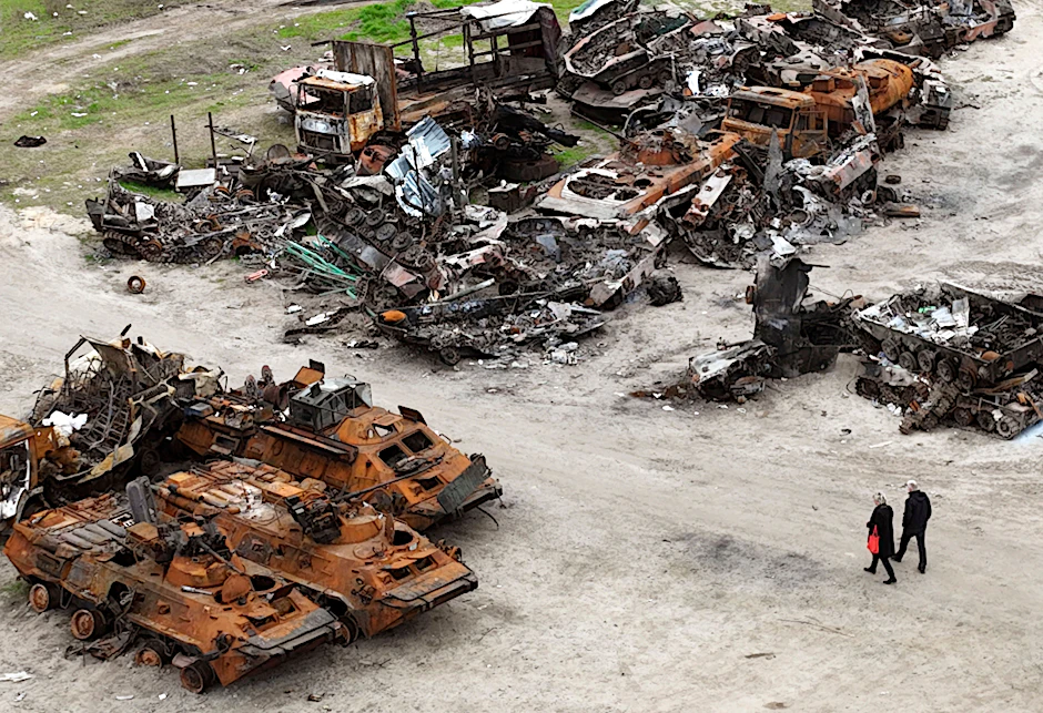 Menschen gehen in Butscha an Wracks von Militärfahrzeugen vorbei.