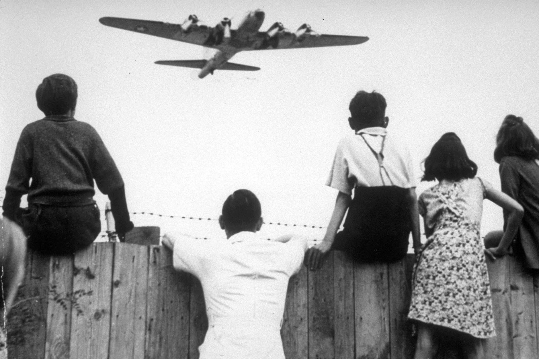 Das im Jahre 1948 aufgenommene Bild zeigt Berliner Kinder am Flughafen Tempelhof während ein Bomber der US-Luftstreitkräfte zur Landung ansetzt.