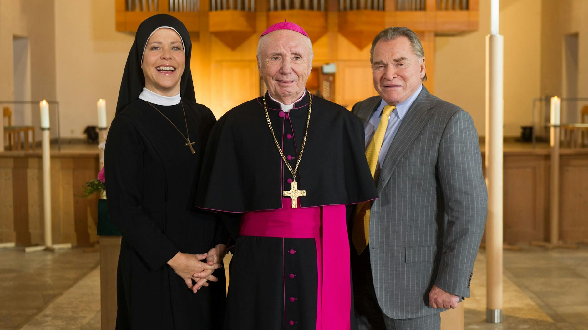Die Schauspieler Janina Hartwig (als Schwester Hanna Jakobi), Horst Sachtleben (als Bischof Rossbauer) und Fritz Wepper (als Wolfgang Wöller) stehen bei einem Pressetermin zu Dreharbeiten der ARD-Serie „Um Himmels Willen“ in der evangelischen Himmelfahrtskirche.