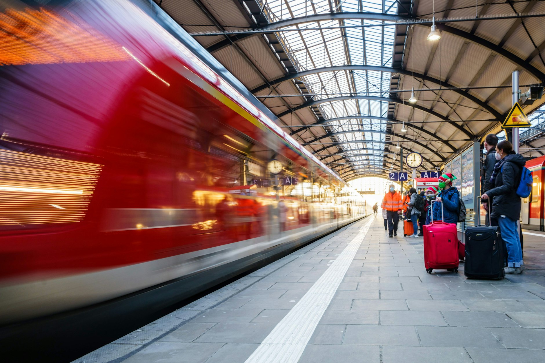 Bahnreisende stehen auf dem Bahnsteig während ein Regionalzug einfährt.
