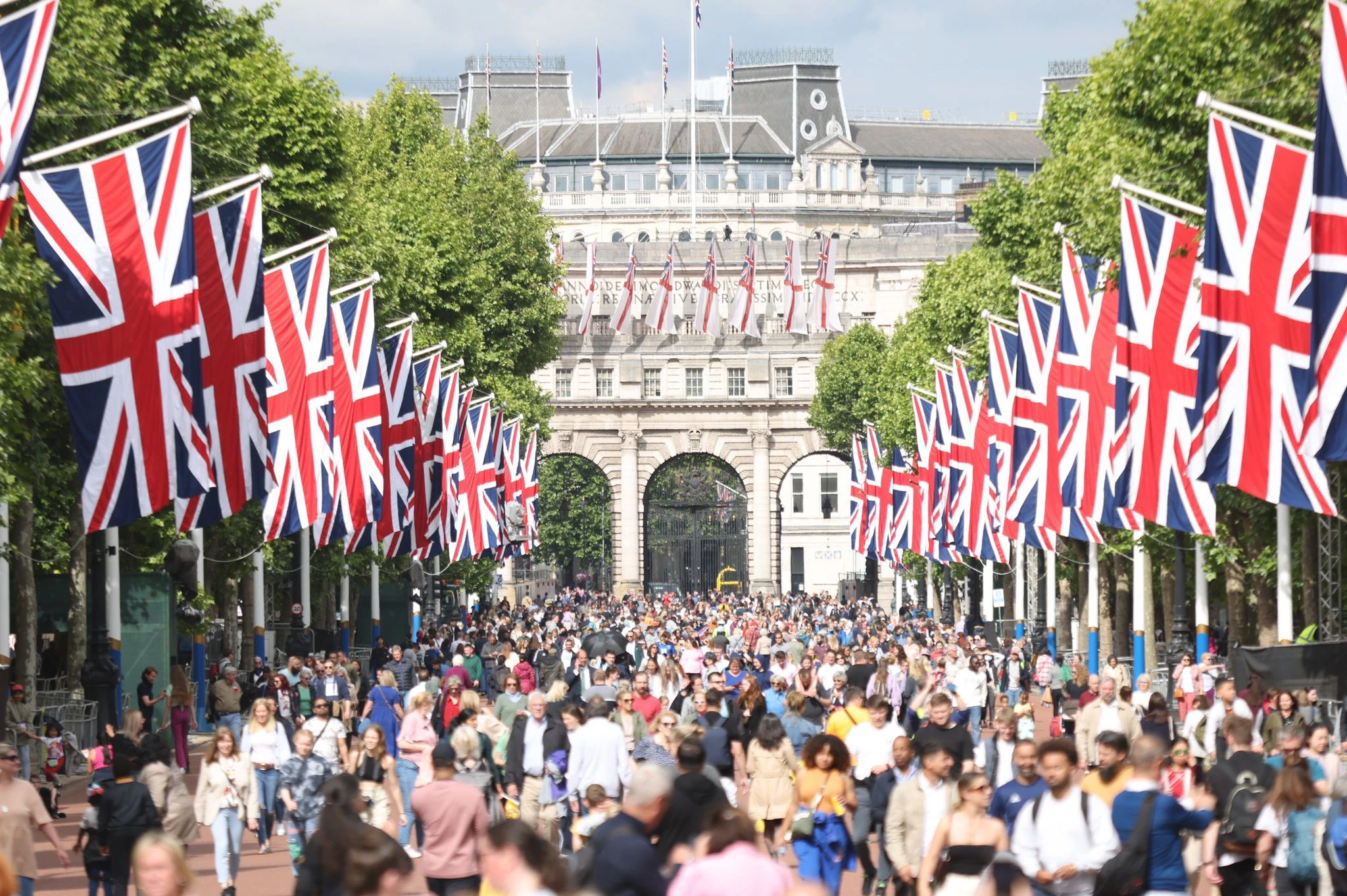Menschen spazieren in London mit Blick auf den Buckingham Palast, während die Straße mit britischen Flaggen gesäumt ist. Einige Gratulanten campieren bereits, um die besten Plätze für die Feierlichkeiten zum Platin-Jubiläum der Queen zu ergattern.  