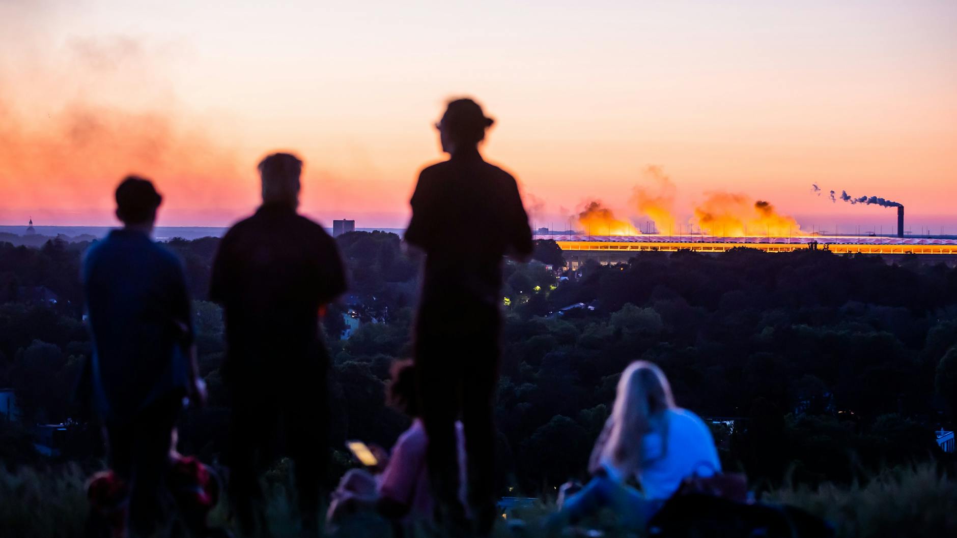 Menschen beobachten vom Drachenberg aus, wie Rauch während eines Konzerts der Band Rammstein über dem Olympiastadion Berlin aufsteigt.