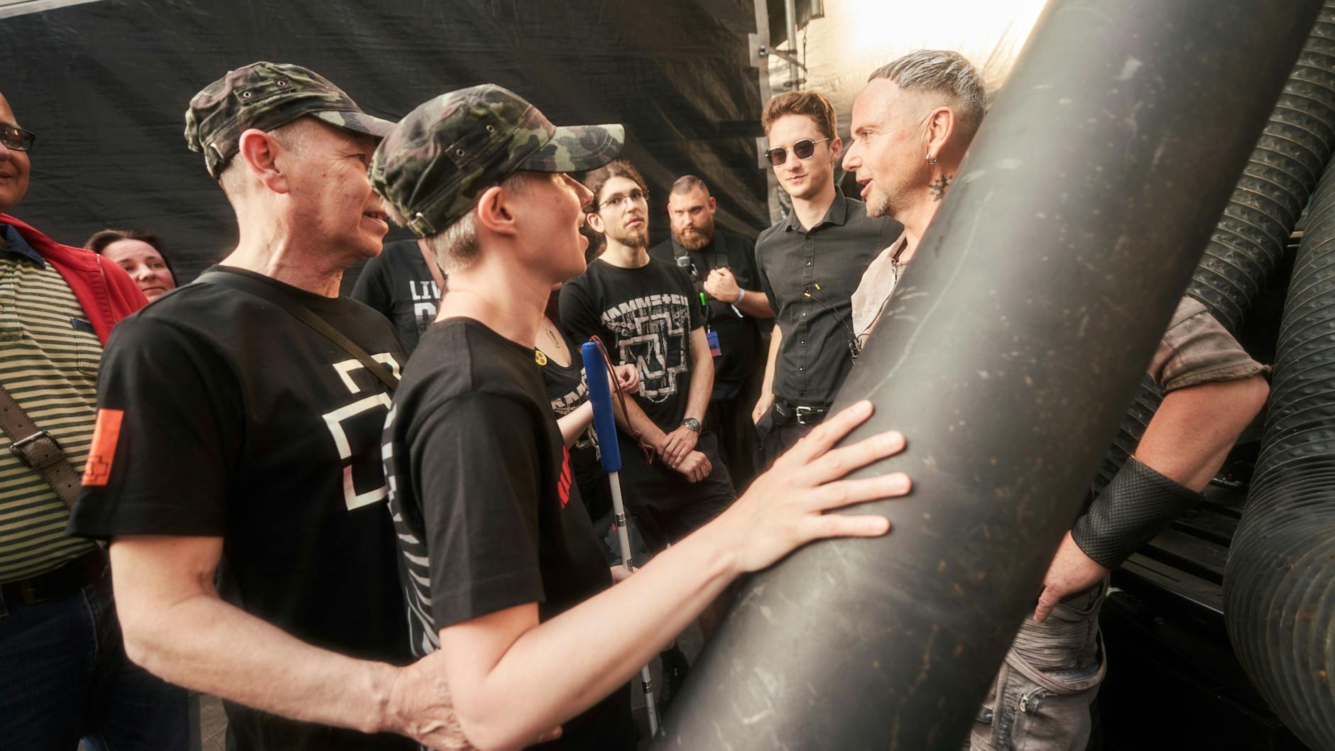 Die blinde Jasmin Wenz betastet eine Stahlstütze hinter der Bühne im Olympiastadion, Rammstein-Gitarrist Paul Landers (re.) erklärt den Bühnenaufbau.