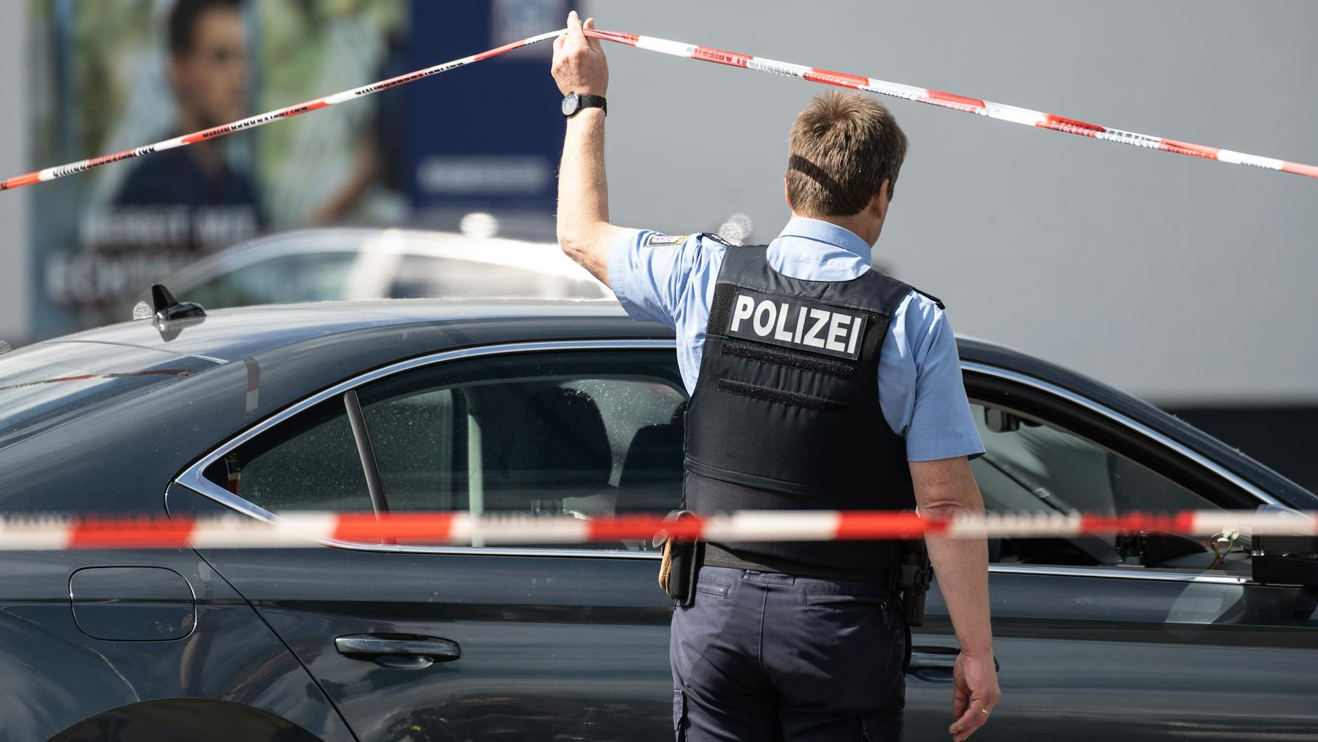 Schwalmstadt: Ein Polizist geht unter einem Absperrband durch, das vor dem betreffenden Einkaufsmarkt befestigt ist.