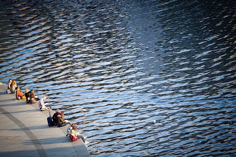 Menschen genießen den Sonnenschein am Ufer der Spree im Regierungsviertel.