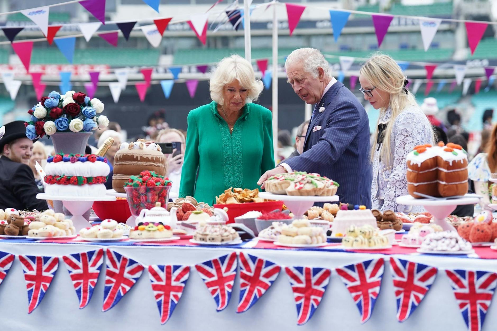Charles (l), Prinz von Wales, und Camilla, Herzogin von Cornwall, begutachten das Kuchenbuffet.