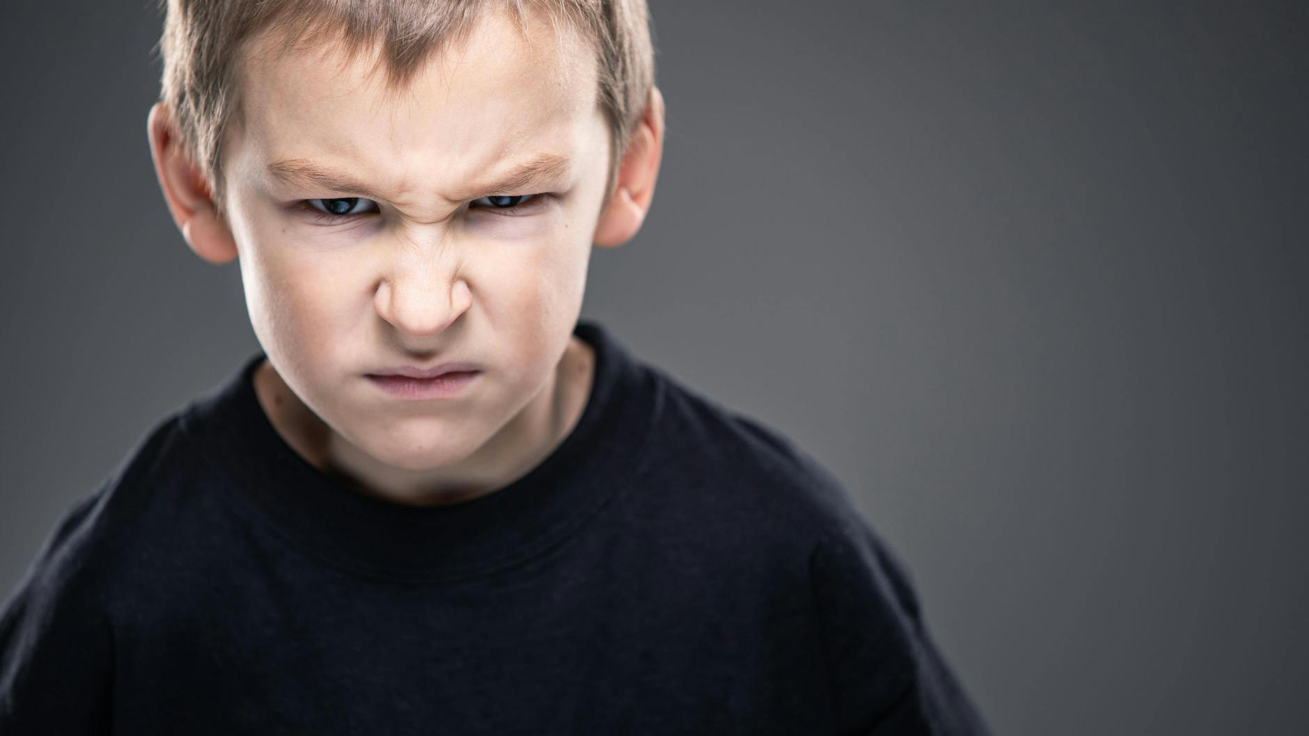 Ein Schüler mit finsterem Gesichtsausdruck. - Wenn der einen anderen Schüler beleidigt, wer wird dann zur Raison gezogen? a) Der Schüler. b) Die Eltern. c) Die Lehrerin.