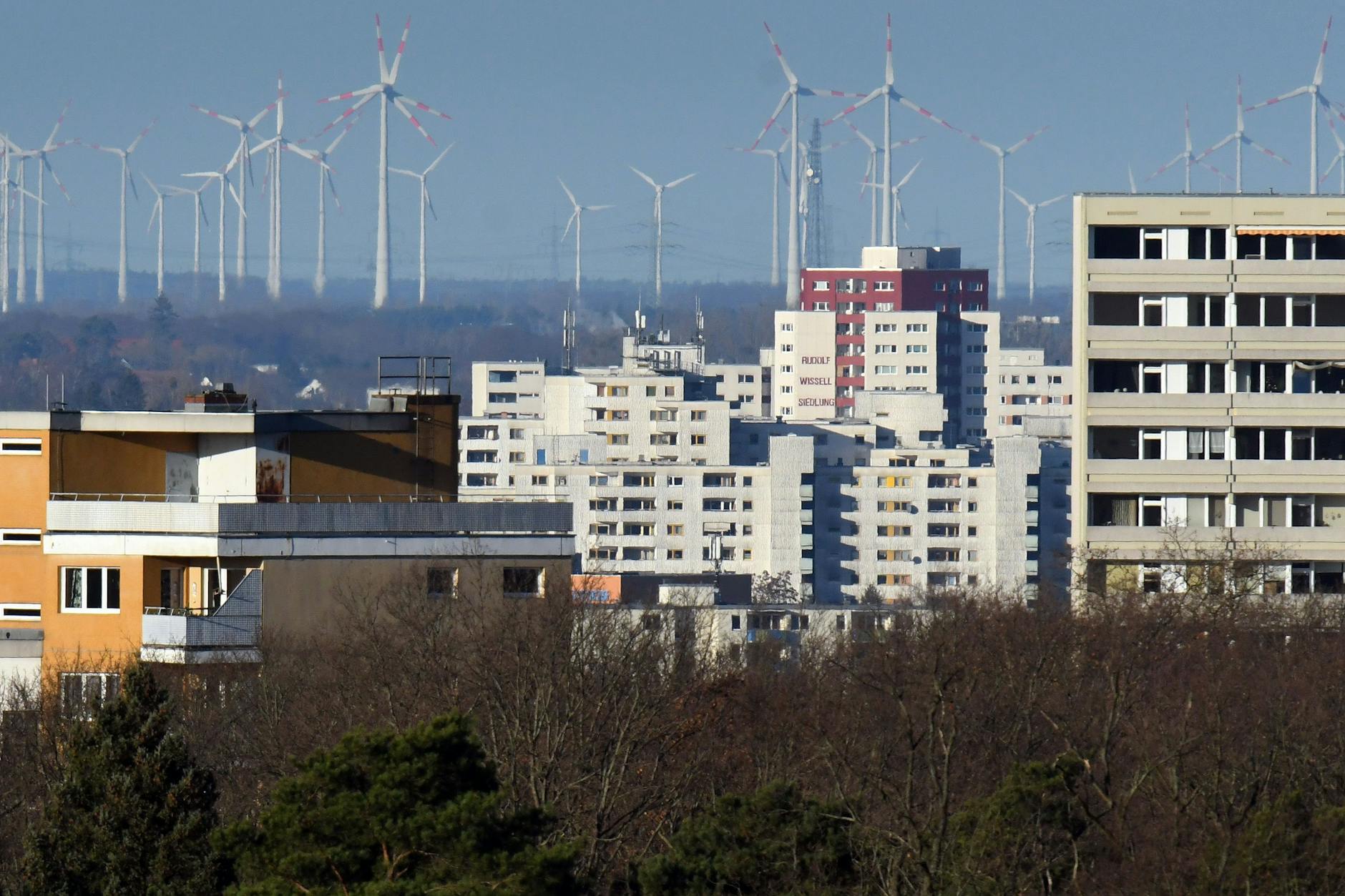 Hochhäuser der Rudolf-Wissell-Siedlung in Spandau. Im Hintergrund Windräder in Brandenburg. Auch in Berlin werden neue Windräder gebaut.