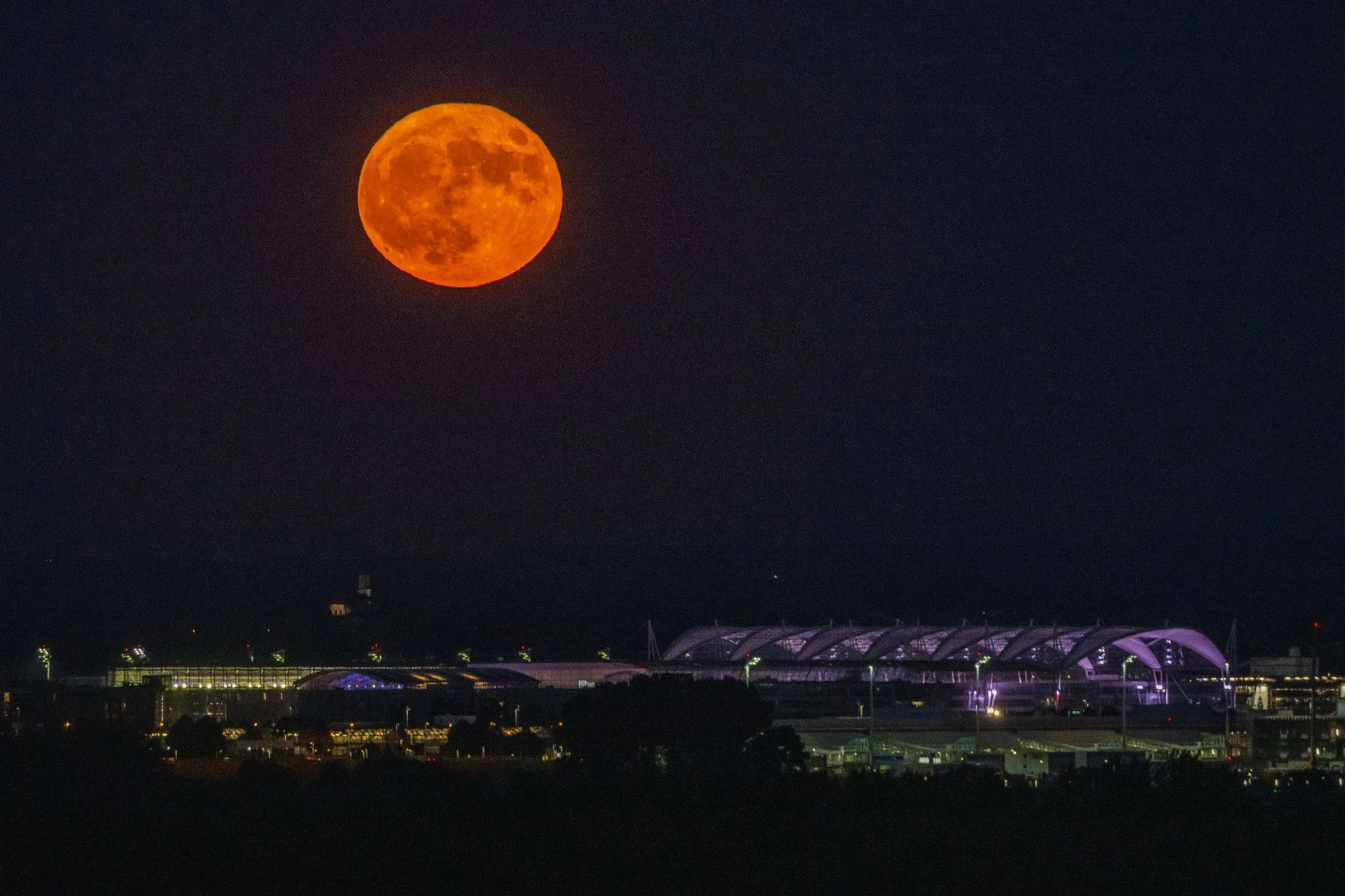 Der rötliche Supermond steht über dem Münchner Flughafen.  