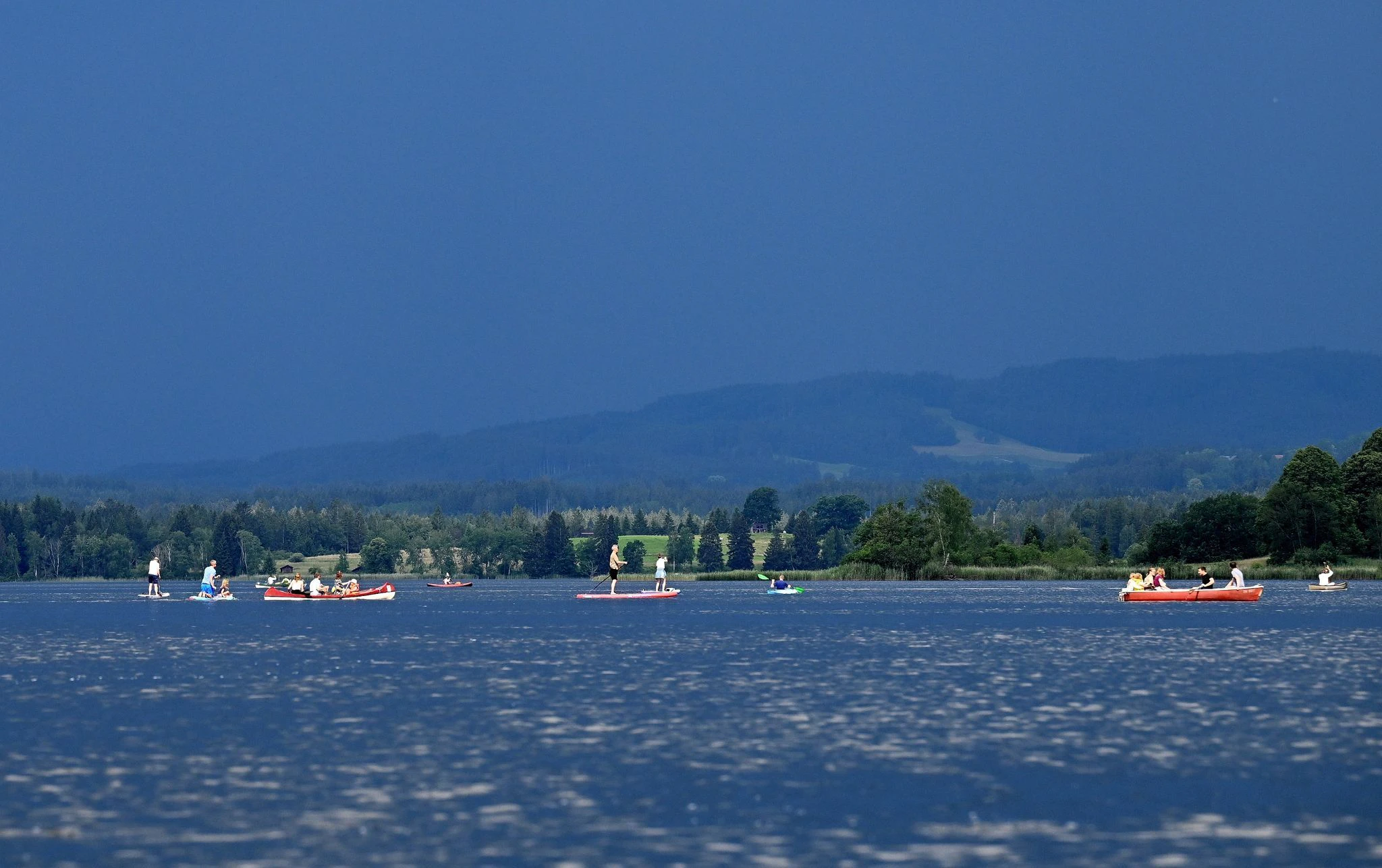 Ausflügler auf dem Wasser flüchten vor einer herannahenden Gewitterfront über dem Staffelsee in Bayern.  