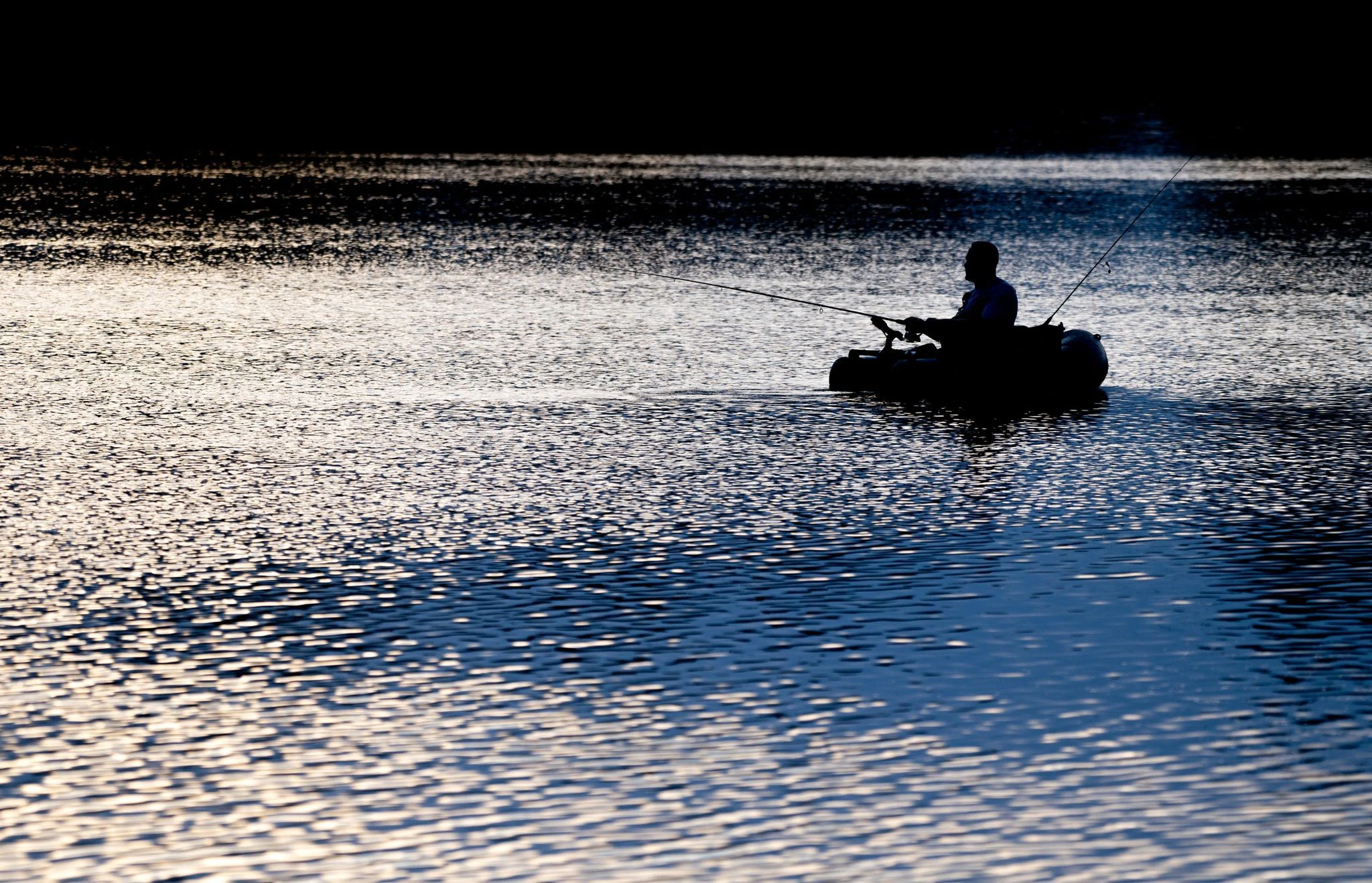 Ein Angler ist kurz nach Sonnenaufgang auf dem Kleinen Bornhorster See in Oldenburg mit einem Schlauchboot unterwegs.  