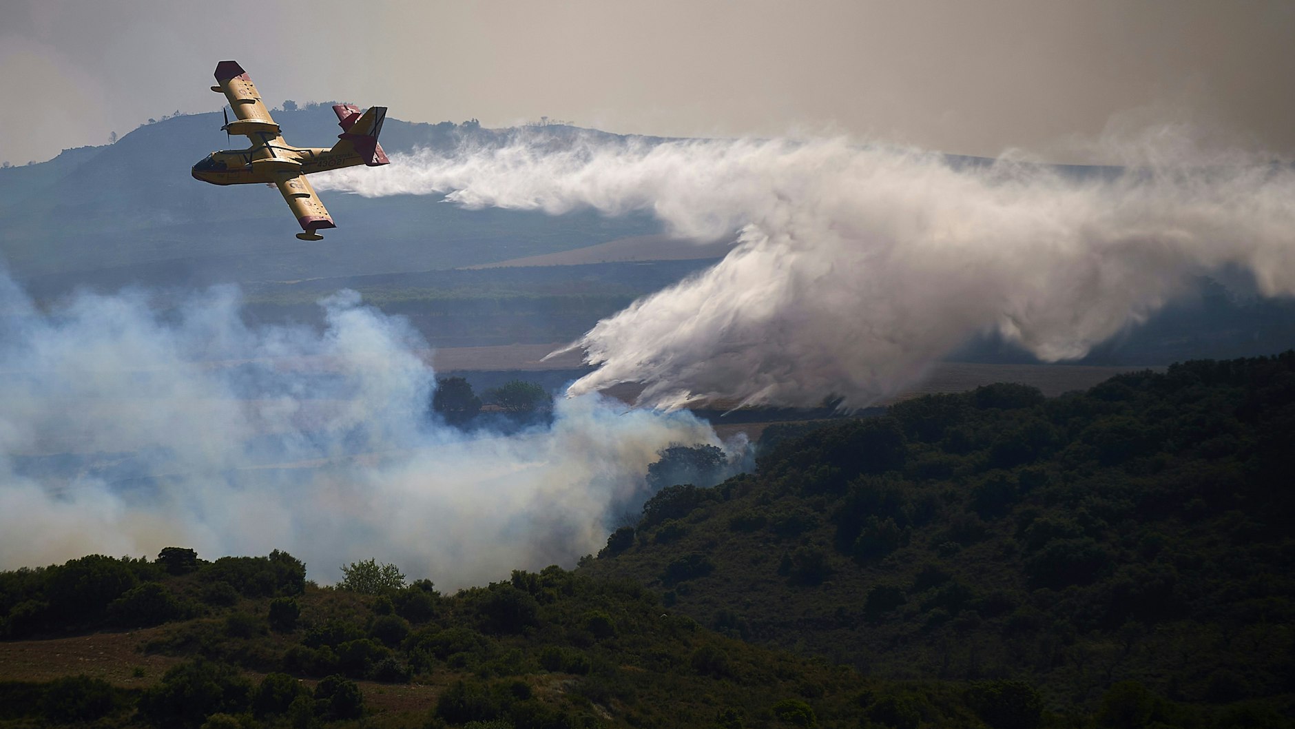 Spanien, San Martin De Unx: Ein Löschflugzeug wirft ein Feuerschutzmittel auf ein brennendes Gebiet ab. Die spanische Feuerwehr kämpft in mehreren Teilen des Landes, die von einer für diese Jahreszeit ungewöhnlichen Hitzewelle betroffen sind, um die Eindämmung von Waldbränden.