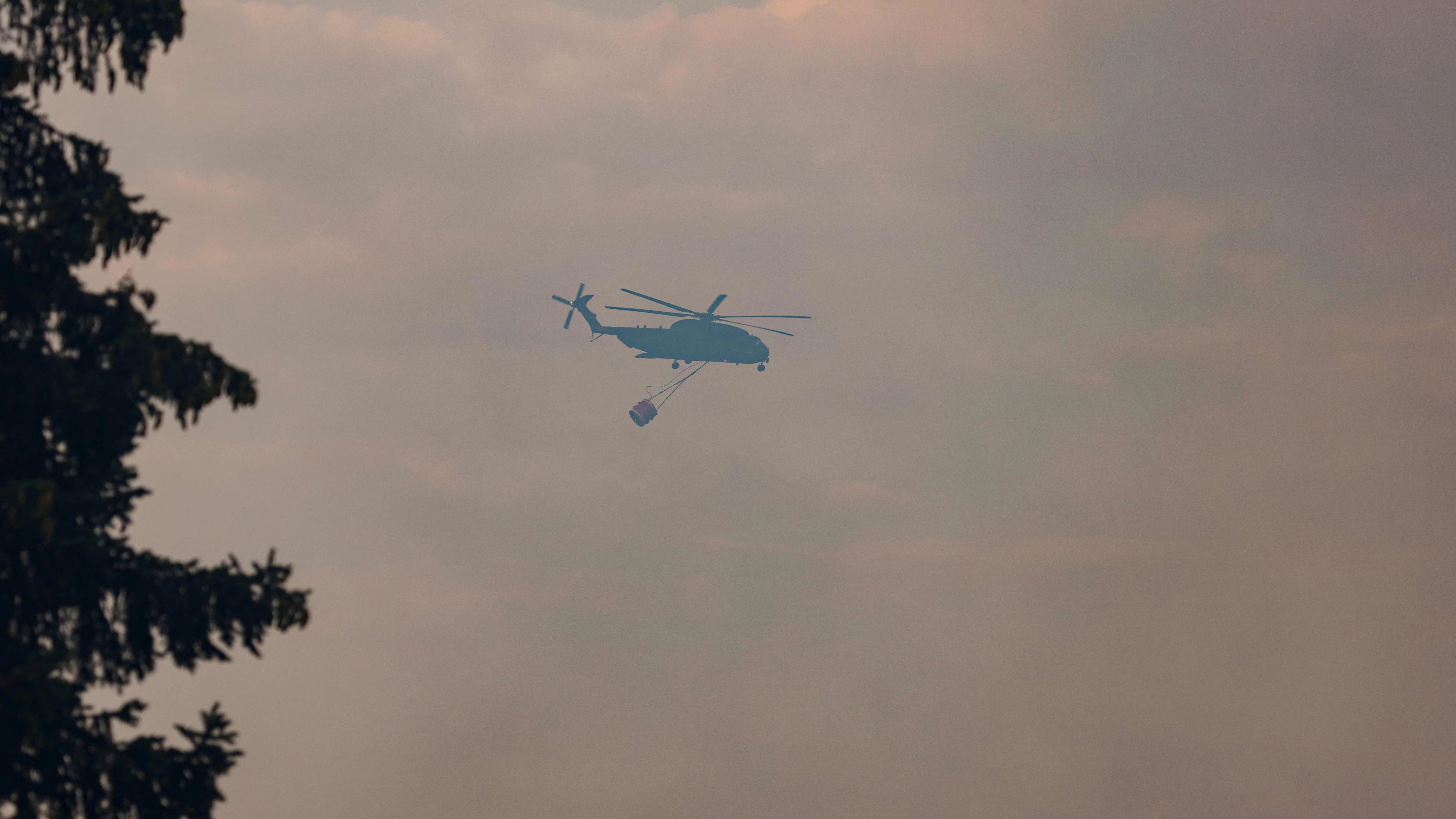 Hubschrauber werfen Löschwasser über den Waldbrandgebieten ab.