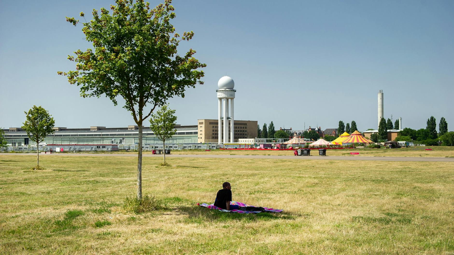 Ein Bild wie aus der Sahelzone: Ein Mensch sucht Schutz unter einem der wenigen Bäume auf dem sonnenverbrannten Tempelhofer Feld.