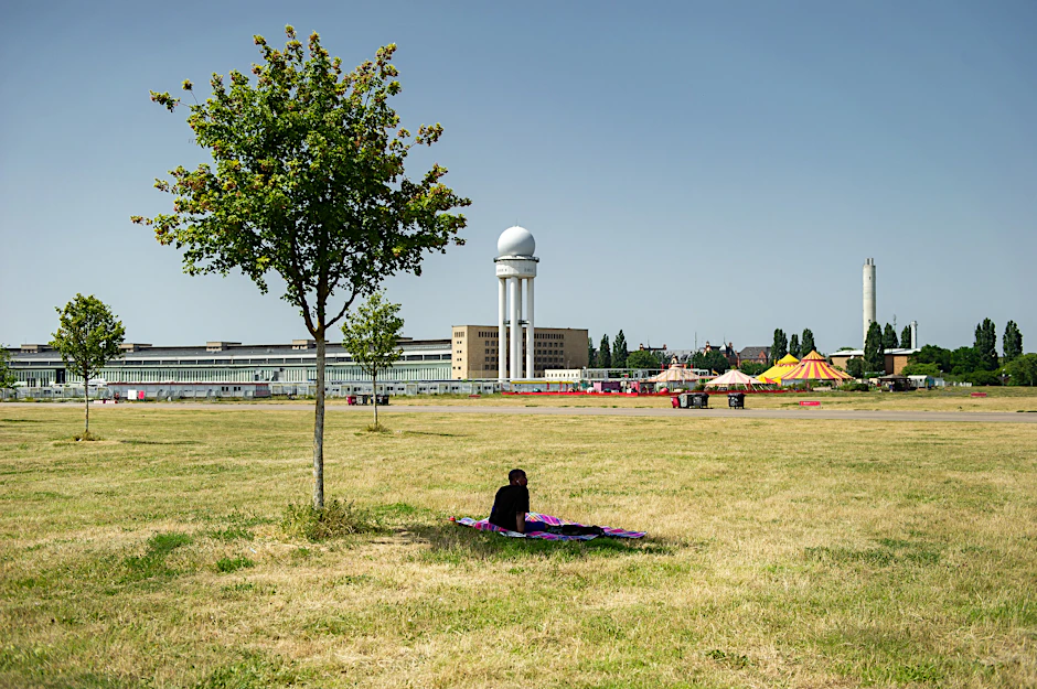 Ein Bild wie aus der Sahelzone: Ein Mensch sucht Schutz unter einem der wenigen Bäume auf dem sonnenverbrannten Tempelhofer Feld.