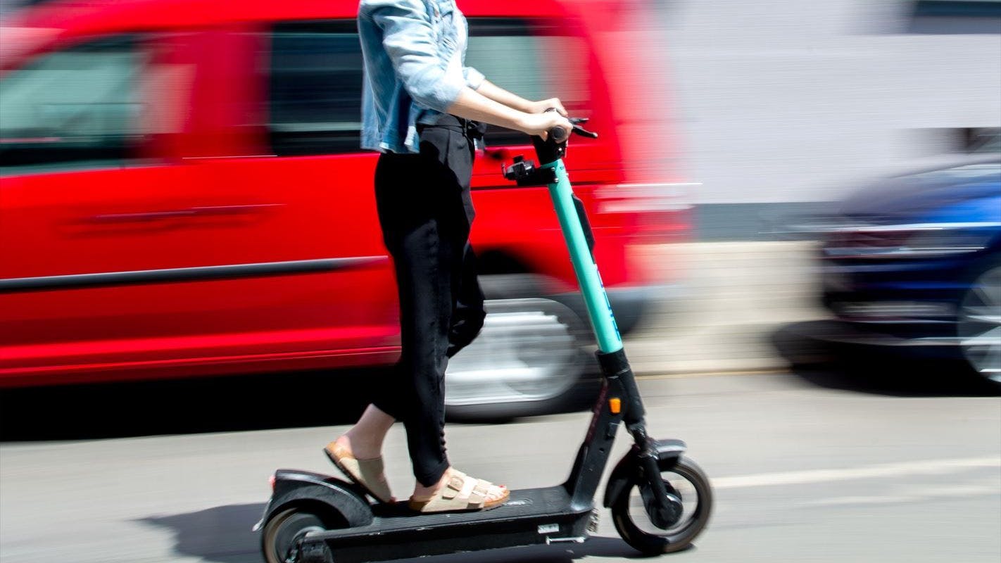 Eine junge Frau düst auf einem E-Scooter an geparkten Autos vorbei. (Symbolbild)
