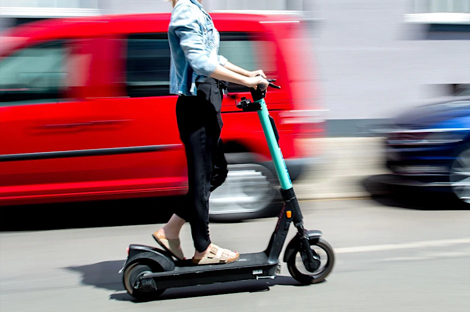Eine junge Frau düst auf einem E-Scooter an geparkten Autos vorbei. (Symbolbild)