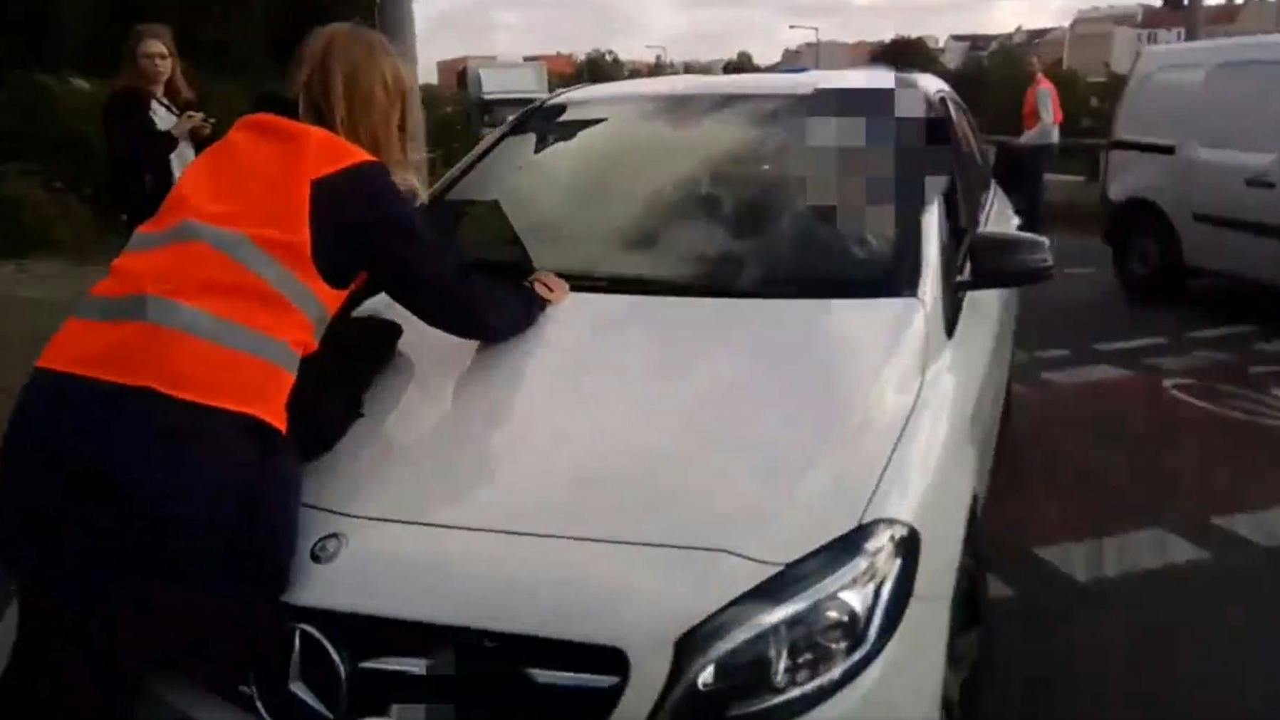 Ein Autofahrer, der nach eigenen Angaben einen Termin hat, fährt trotz Aktivistin langsam weiter.