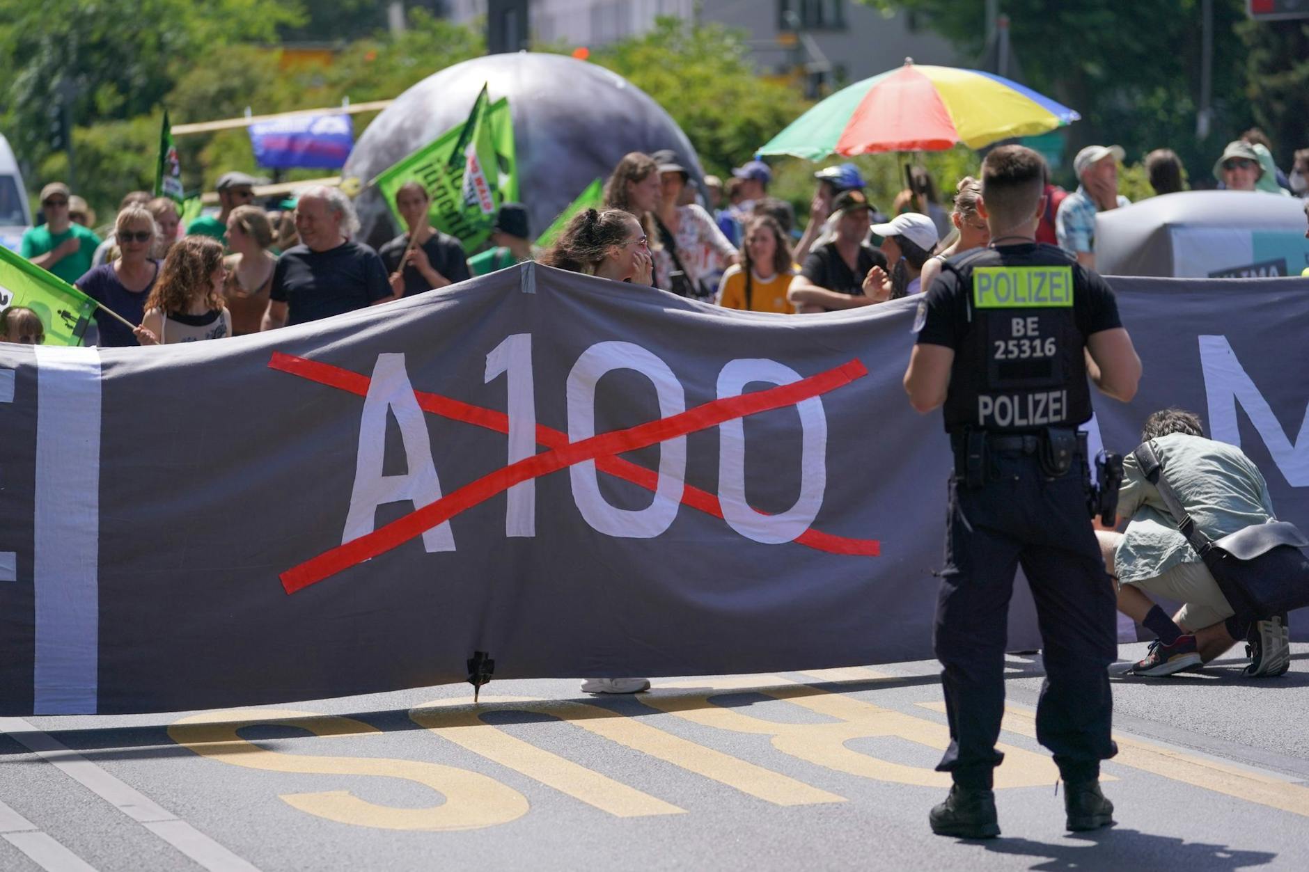 Ein Polizist steht bei einer Demo gegen den Weiterbau der Stadtautobahn A100 vor einem Banner der Demonstranten.