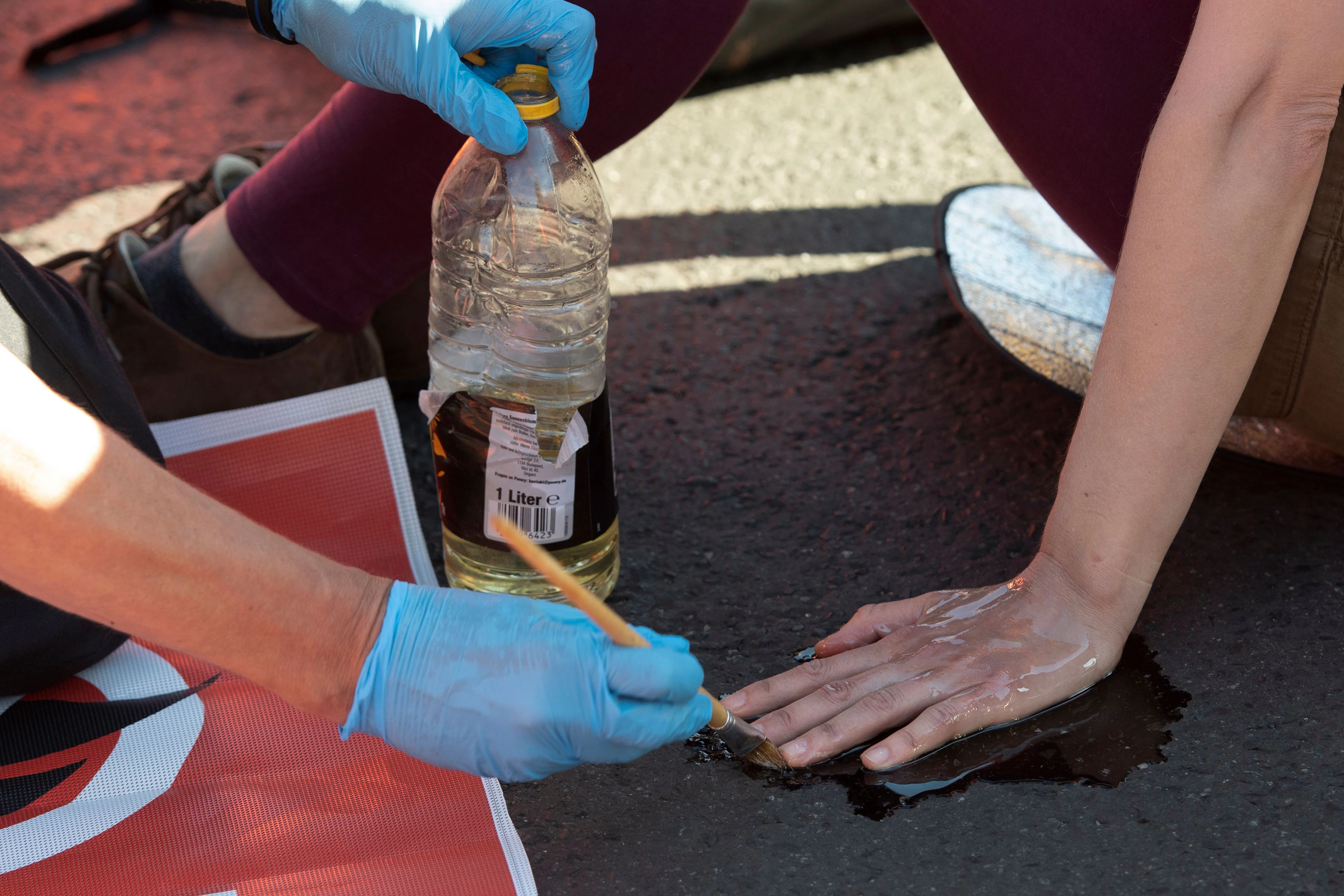 Ein Polizeibeamter löst mit Sonnenblumenöl die festgeklebte Hand eines Klimaschutz-Demonstranten der Gruppe „Letzte Generation“ vom Asphalt auf der Kreuzung am Frankfurter Tor.